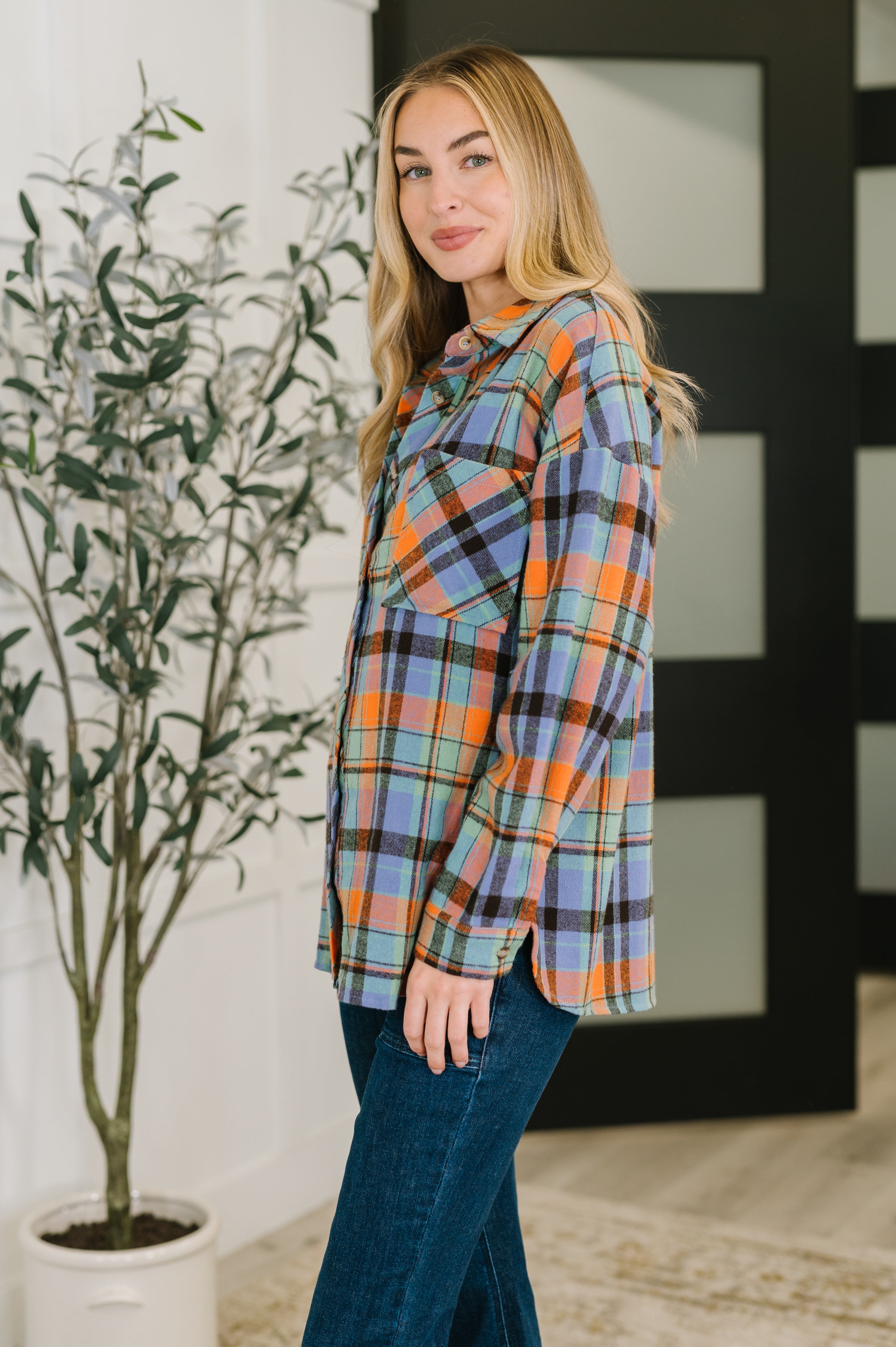 Woman with blonde hair wearing a blue, orange, and green plaid button-down shirt paired with dark jeans indoors