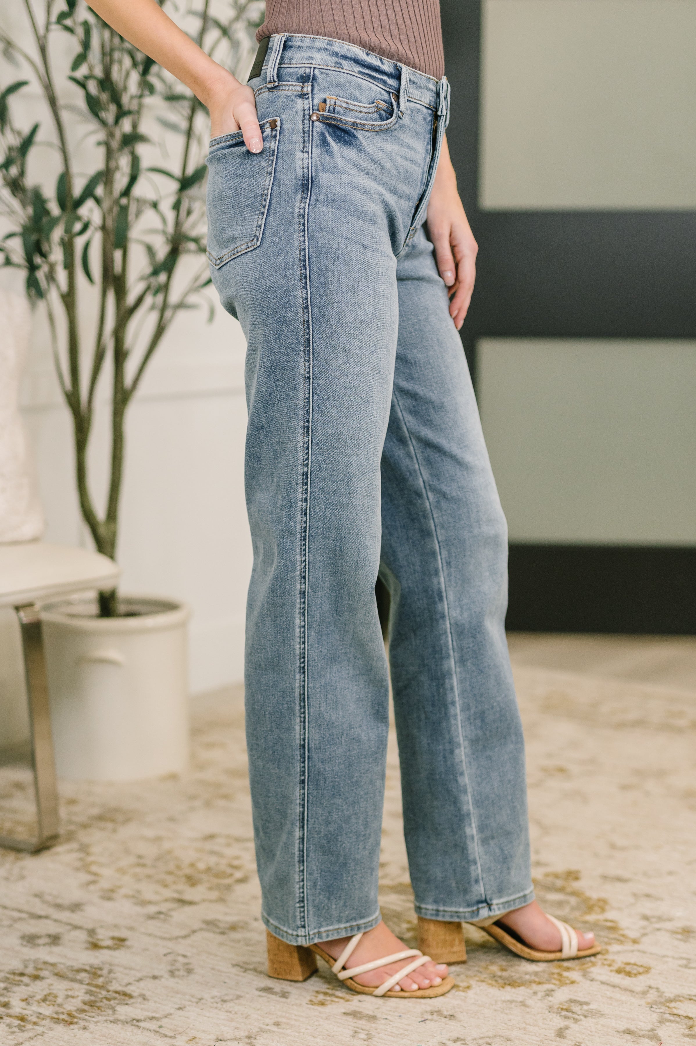 Person wearing blue straight-leg jeans with high waist and beige heeled sandals standing indoors