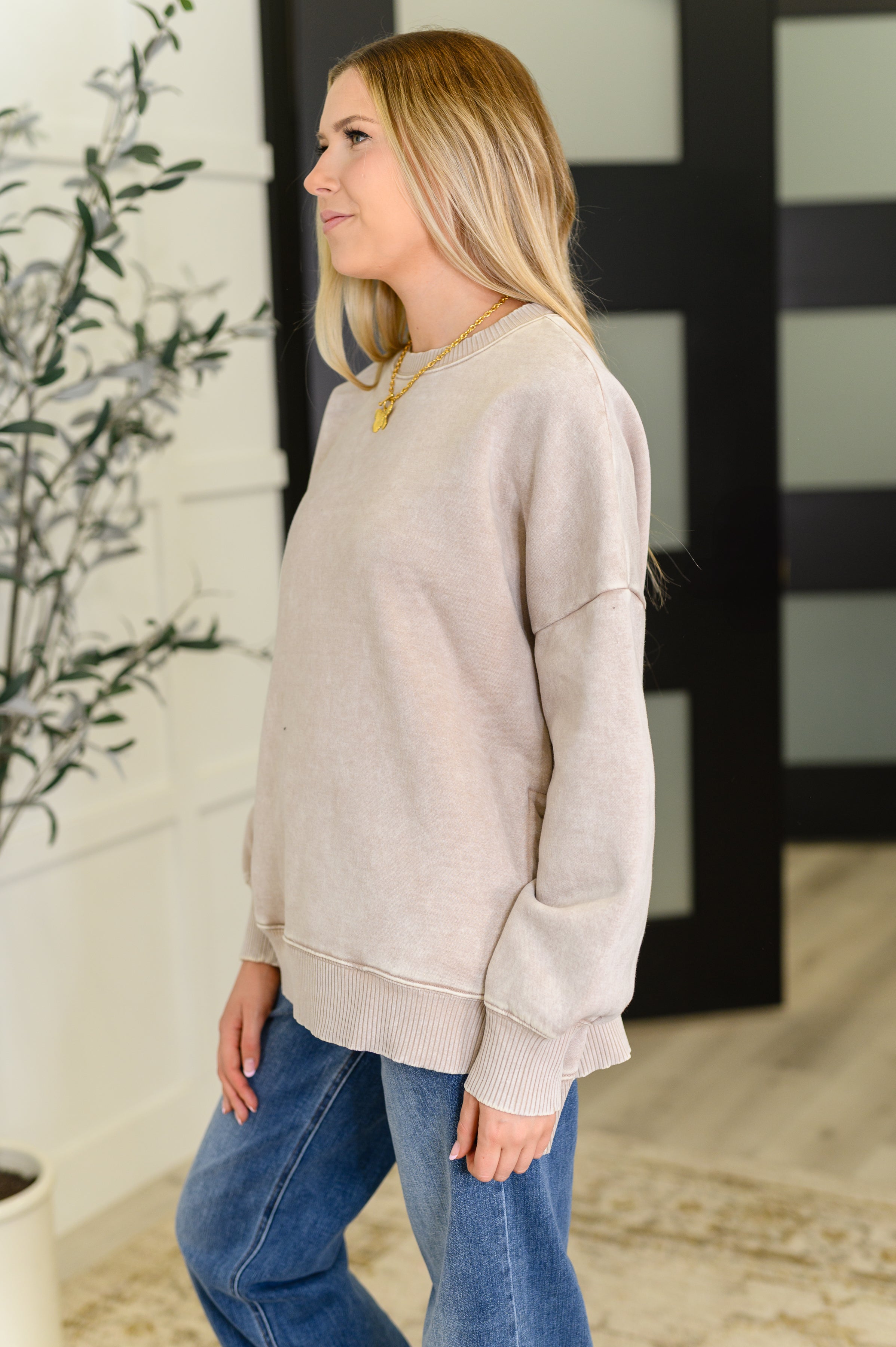 Woman wearing ash mocha mineral wash pullover with relaxed fit paired with blue jeans indoors near plant and door