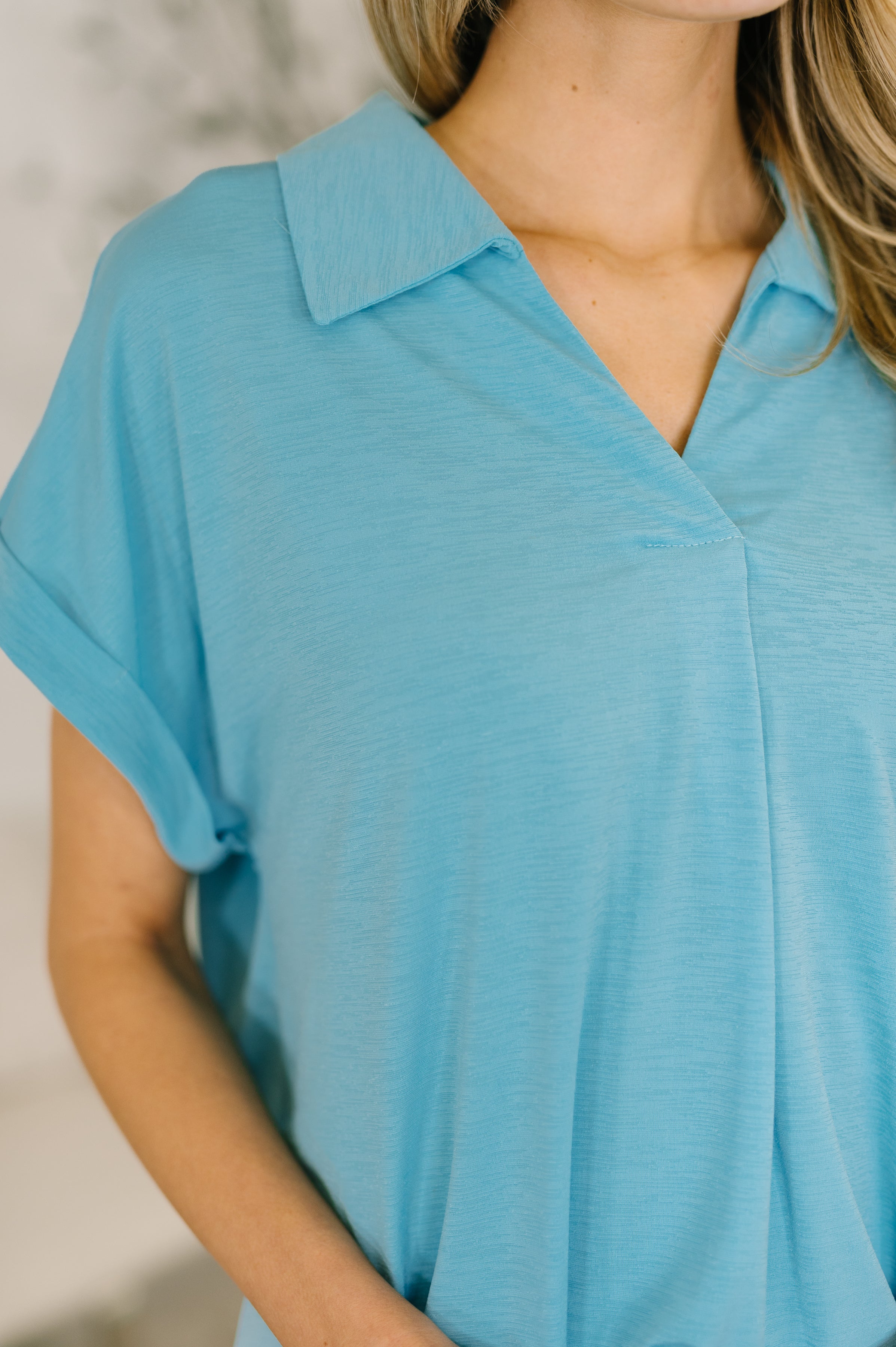Close-up of a coastal blue collared top with V-neckline and rolled short sleeves on model's upper torso