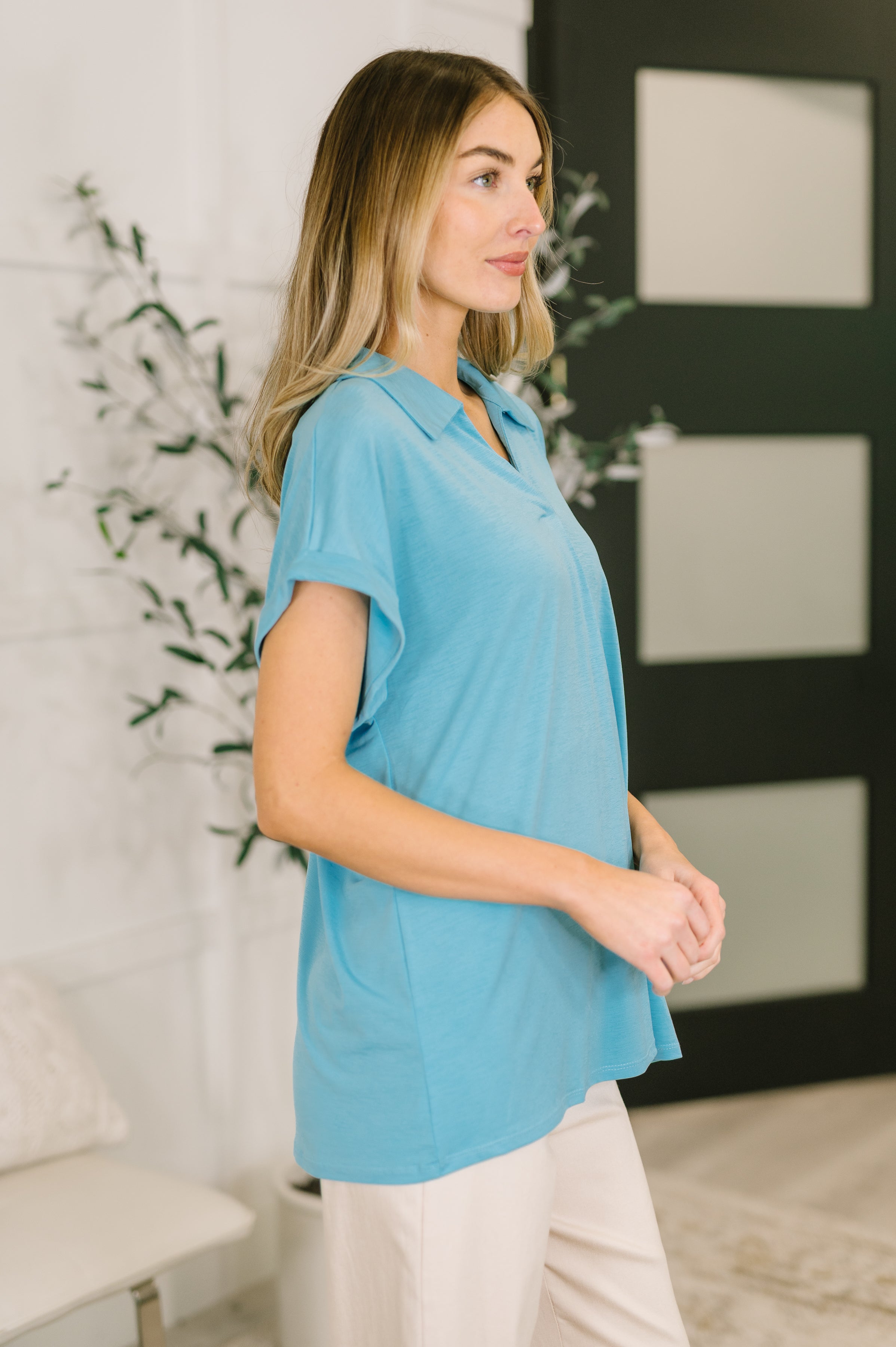 Woman modeling soft coastal blue collared top with short dolman sleeves in bright indoor setting