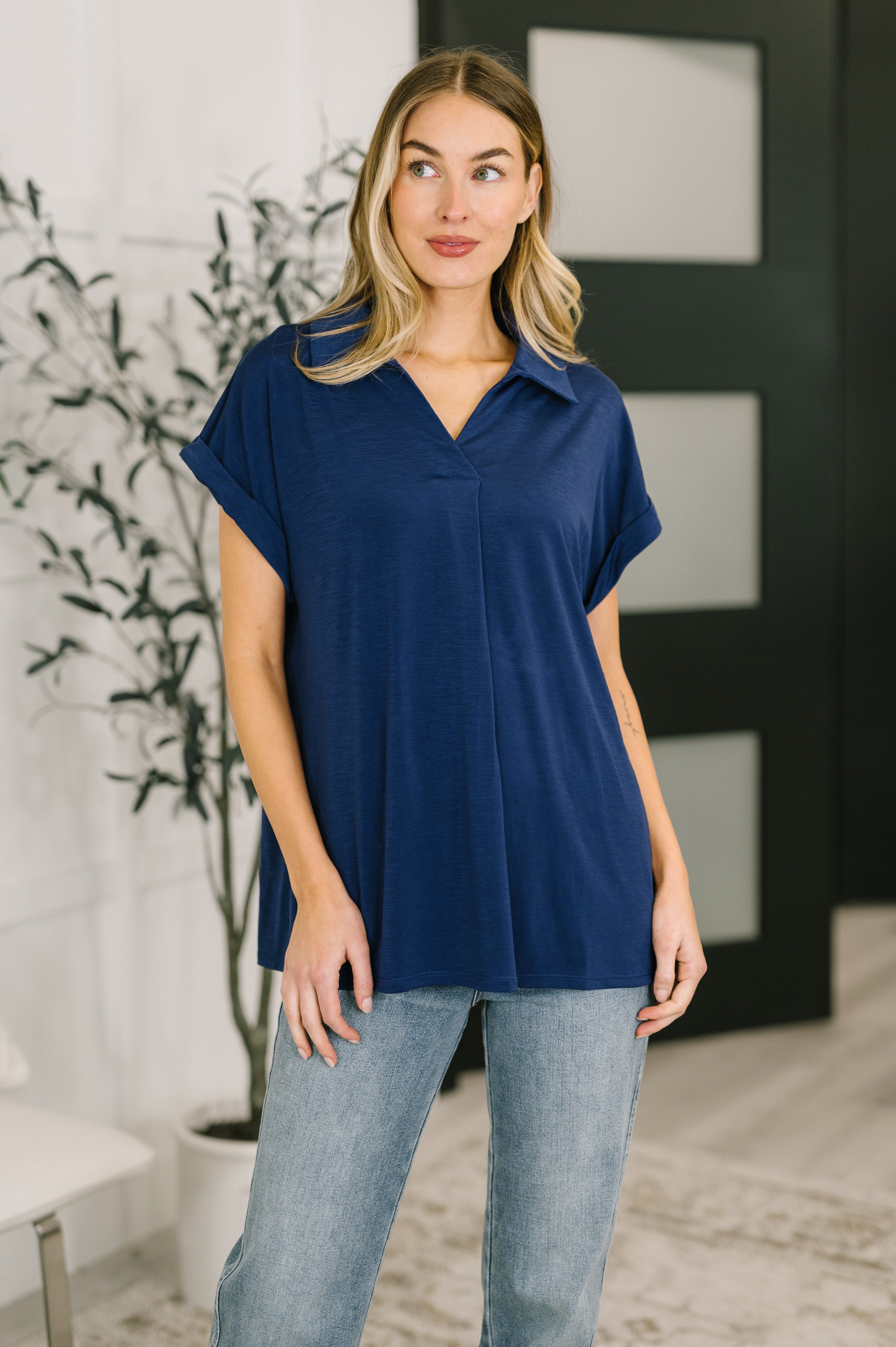 Woman wearing relaxed navy collared top with dolman sleeves and rolled cuffs paired with light wash jeans indoors