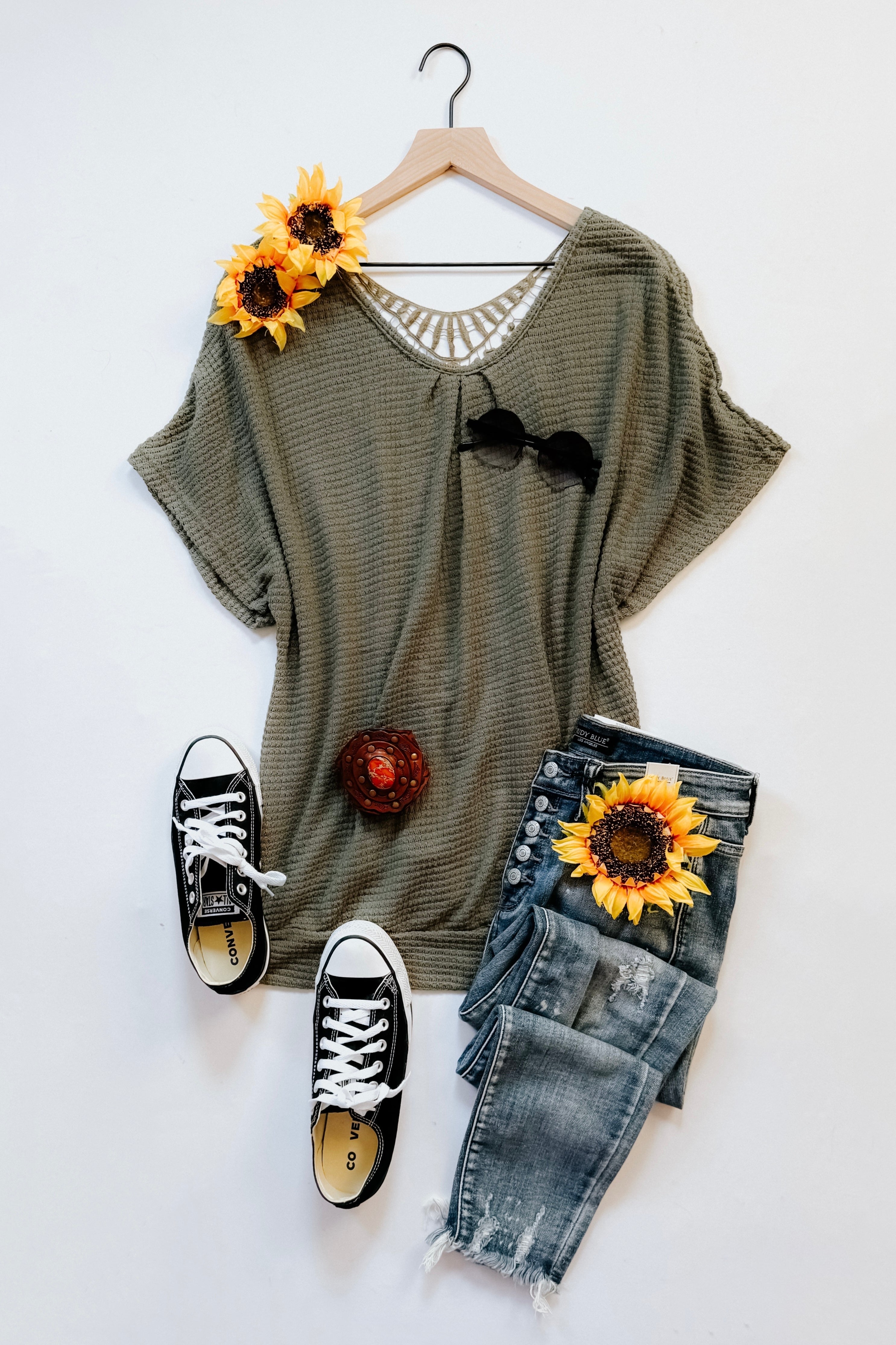 Olive knit top with lace back detail paired with distressed jeans and black low-top sneakers styled with sunflowers