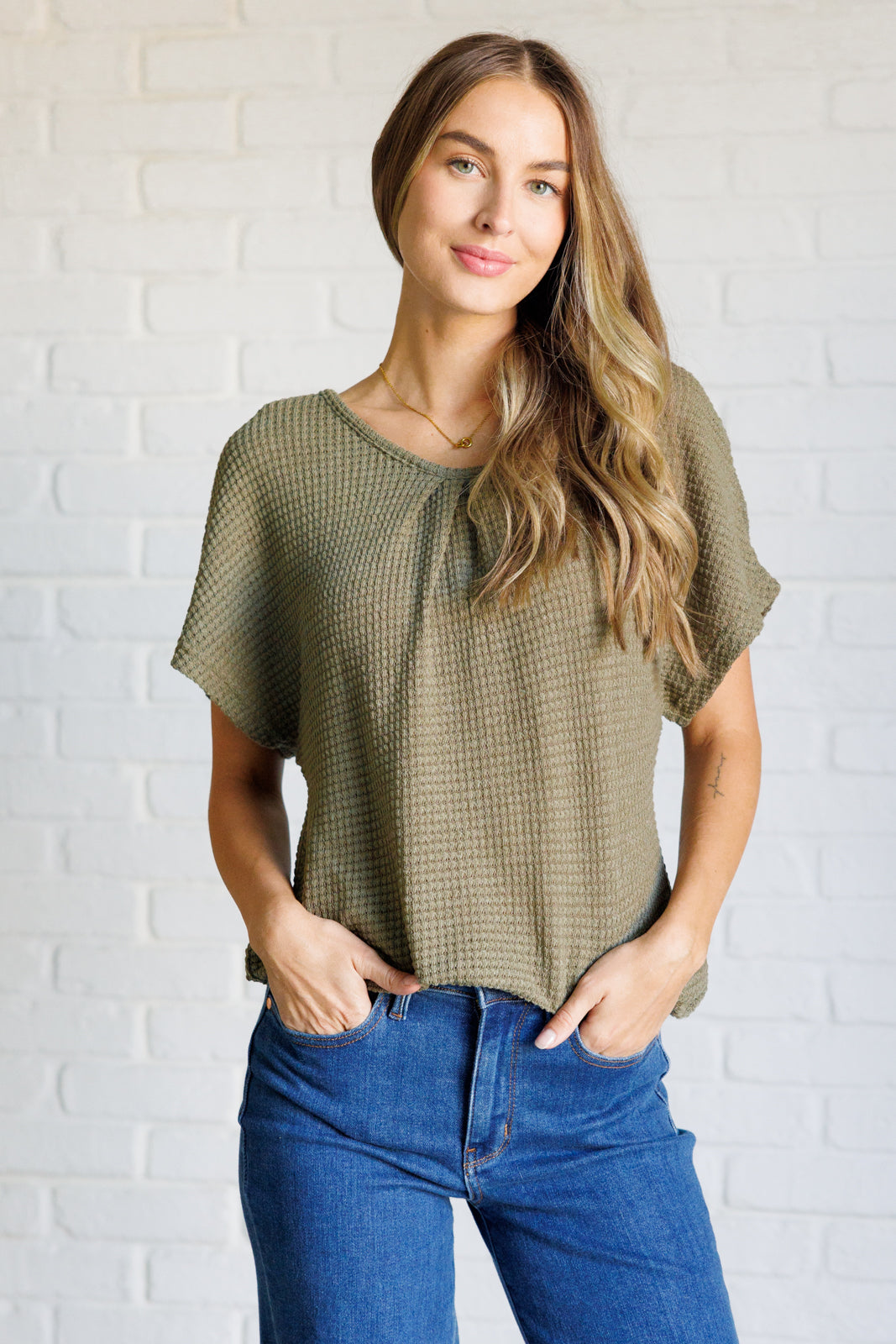 Woman wearing olive textured relaxed-fit top with short sleeves paired with medium wash blue jeans indoors