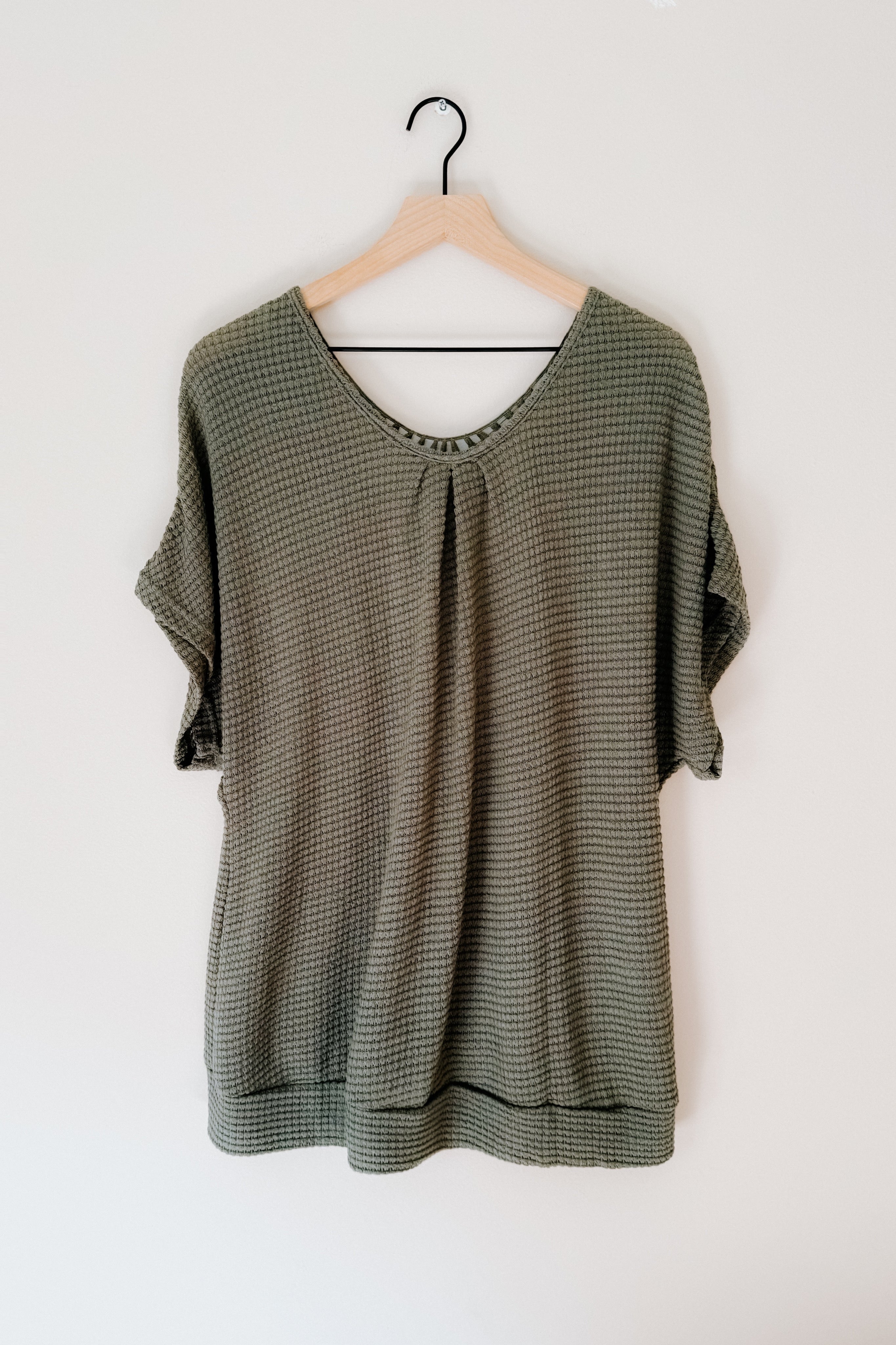 Olive green textured short sleeve top with subtle gathered detail at neckline hanging on wooden hanger