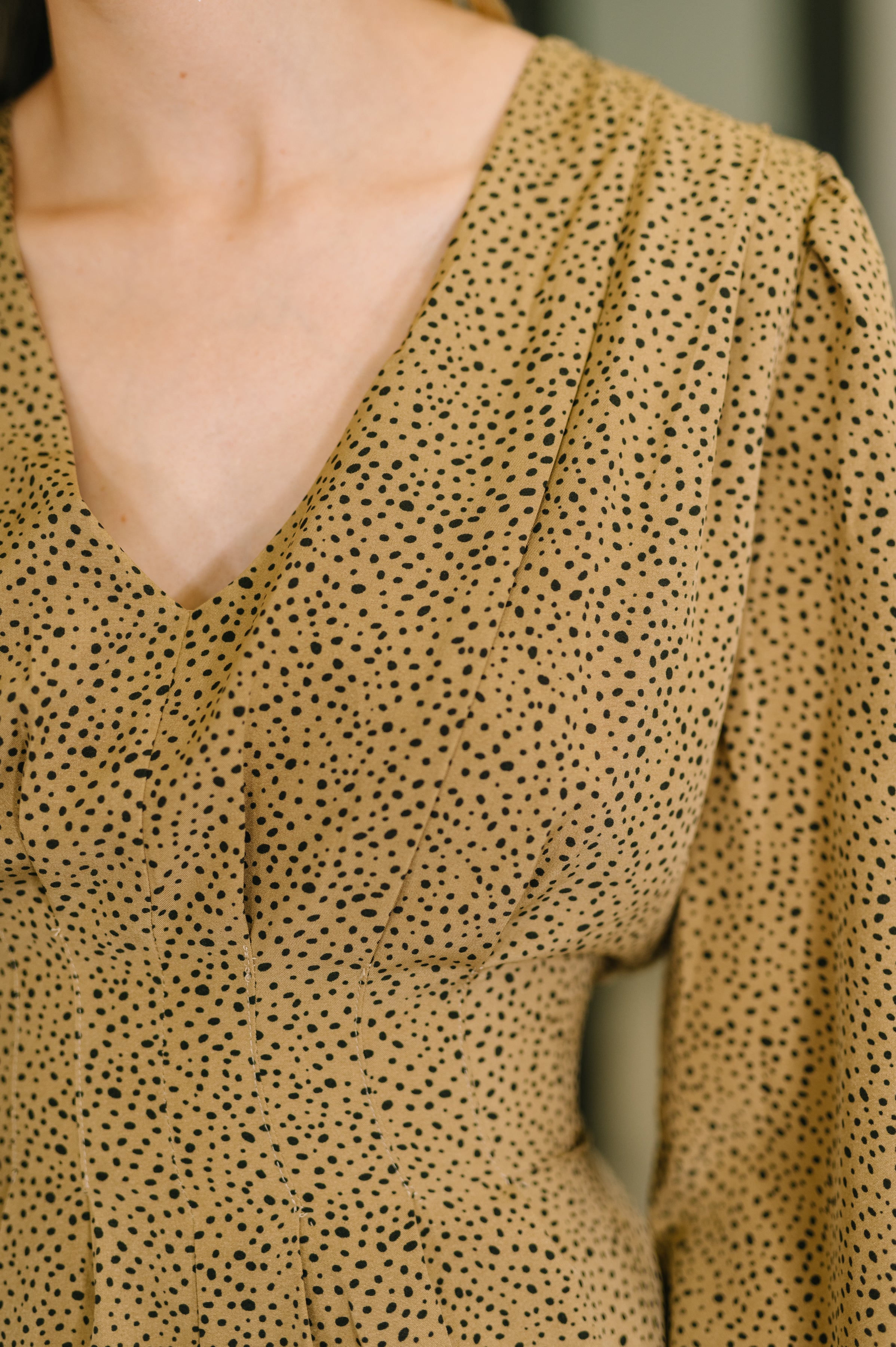 Close-up of tan V-neck dress with small irregular black dots showing neckline and bust seam details