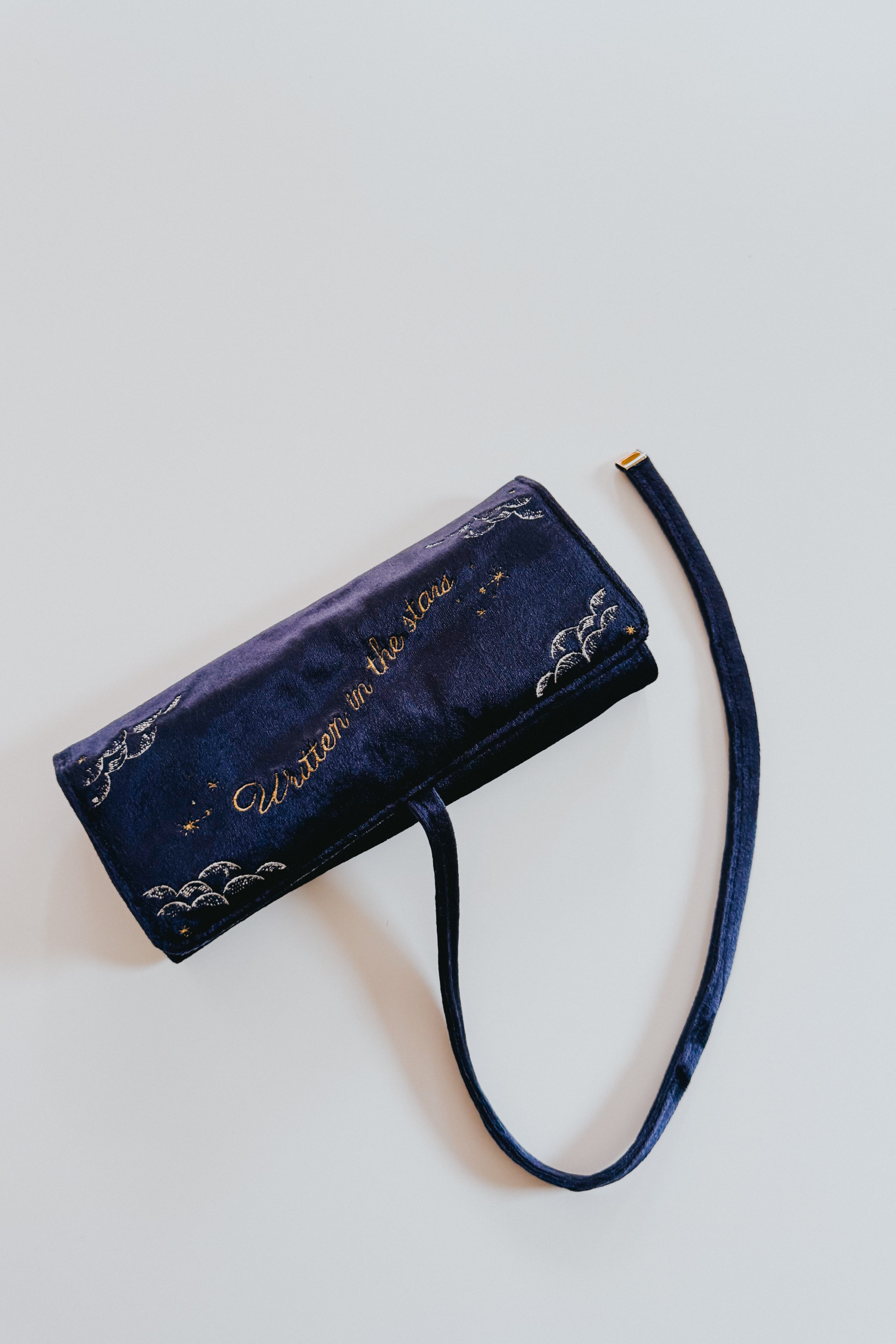 Navy velvet jewelry roll with celestial embroidery and gold text "Unicorn in the stars" laid flat with strap visible