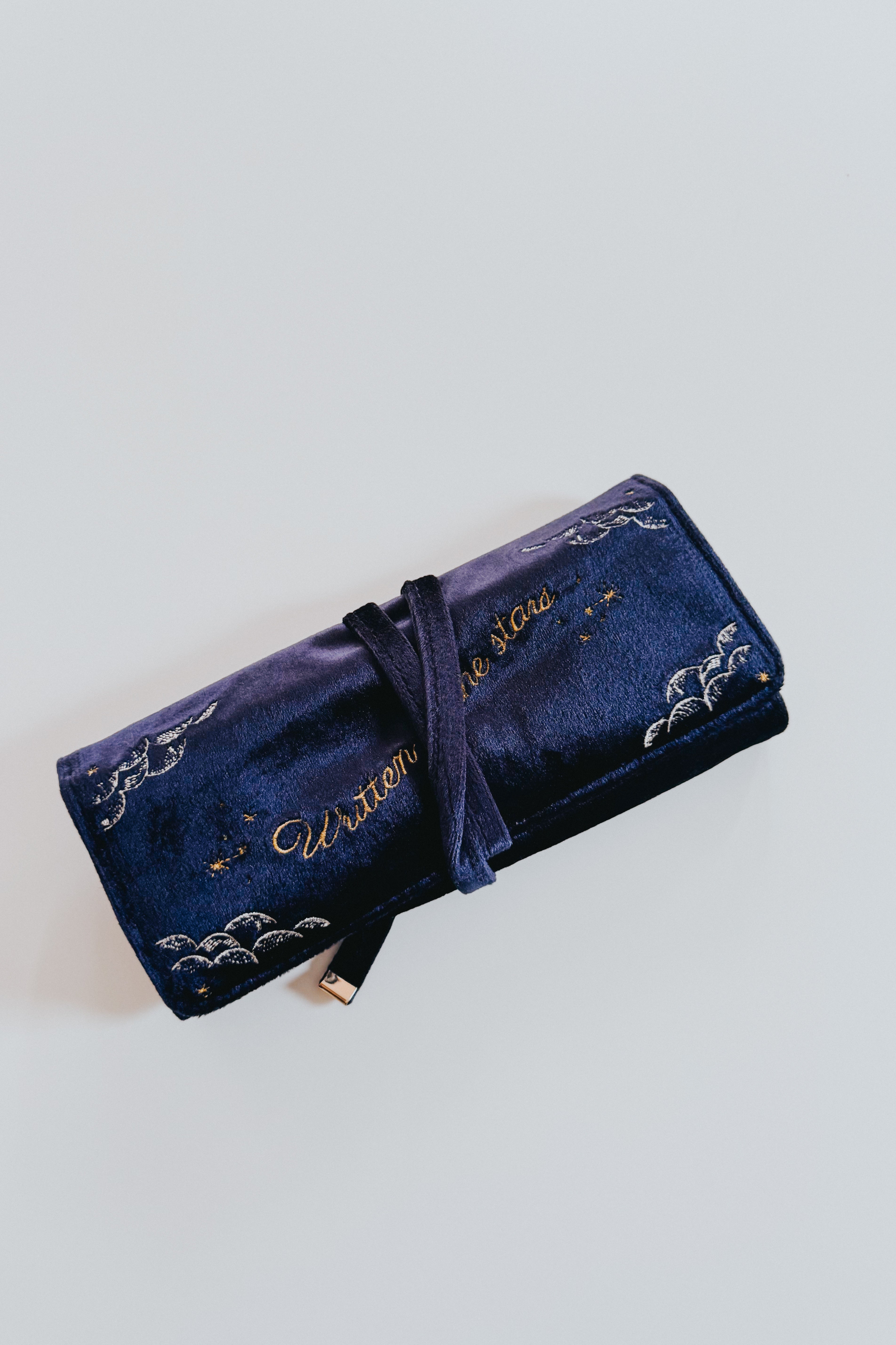 Rolled celestial velvet jewelry organizer in deep blue with silver and gold embroidery and delicate tie closure on neutral background