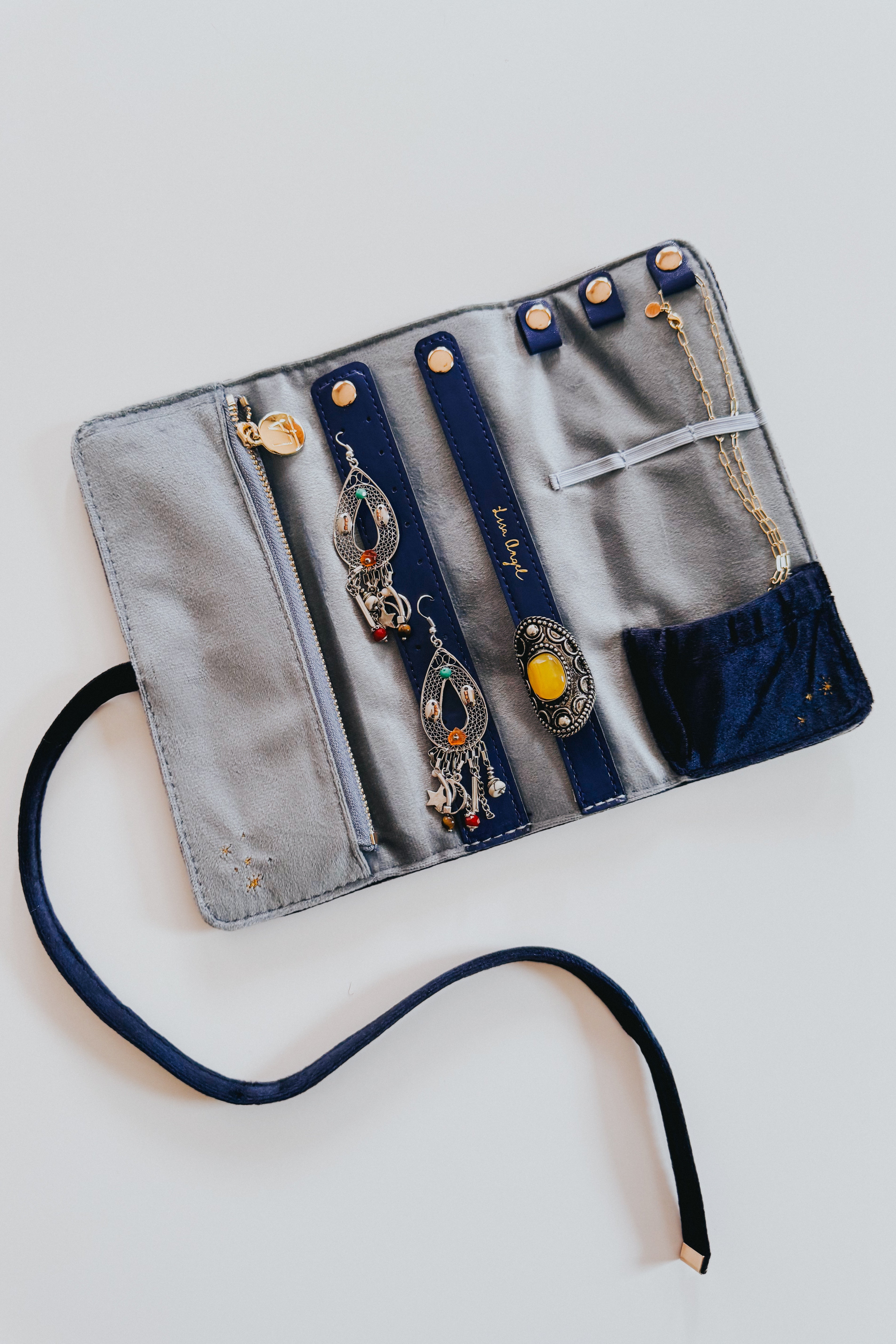 Open blue and navy velvet jewelry roll with earrings, ring, and necklace organized inside on light background