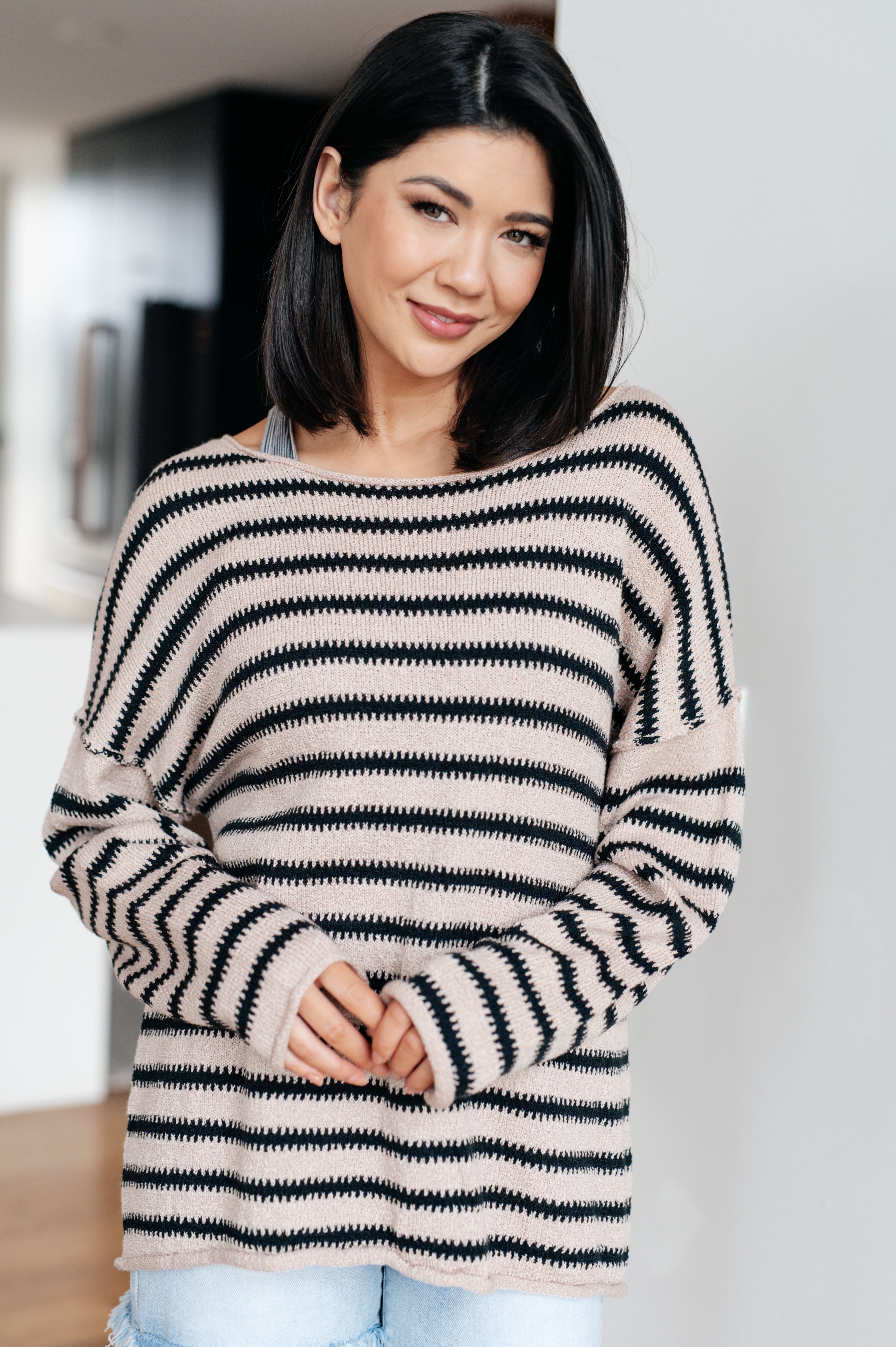 Woman wearing a taupe sweater with black stripes and denim shorts indoors.