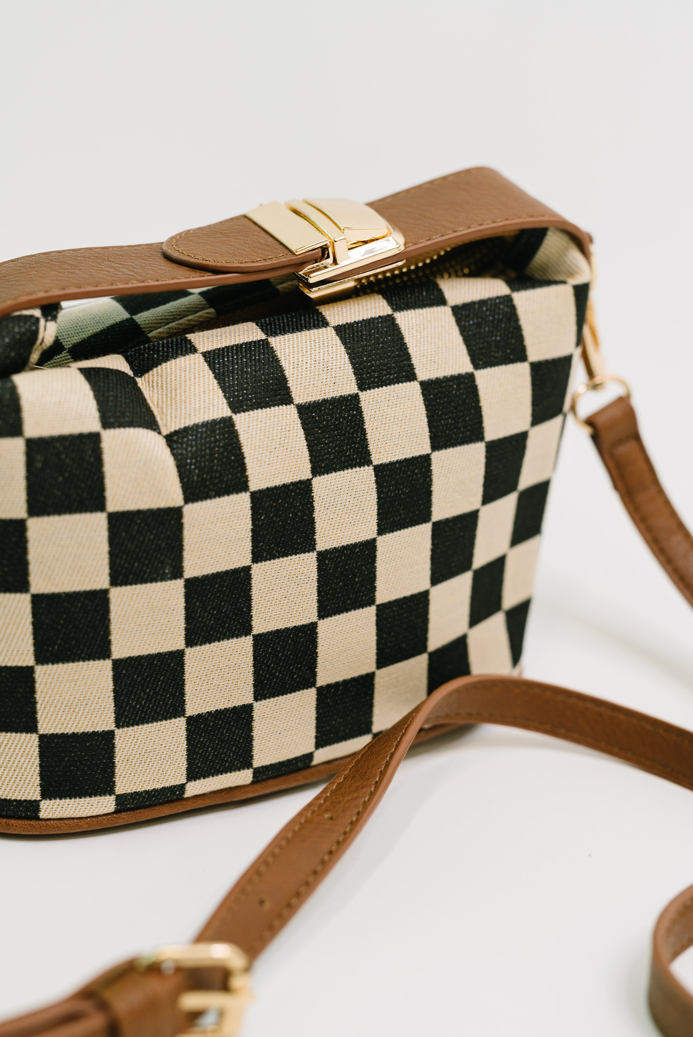 Brown leather and black-and-white checkered crossbody bag with gold hardware and adjustable strap on white background