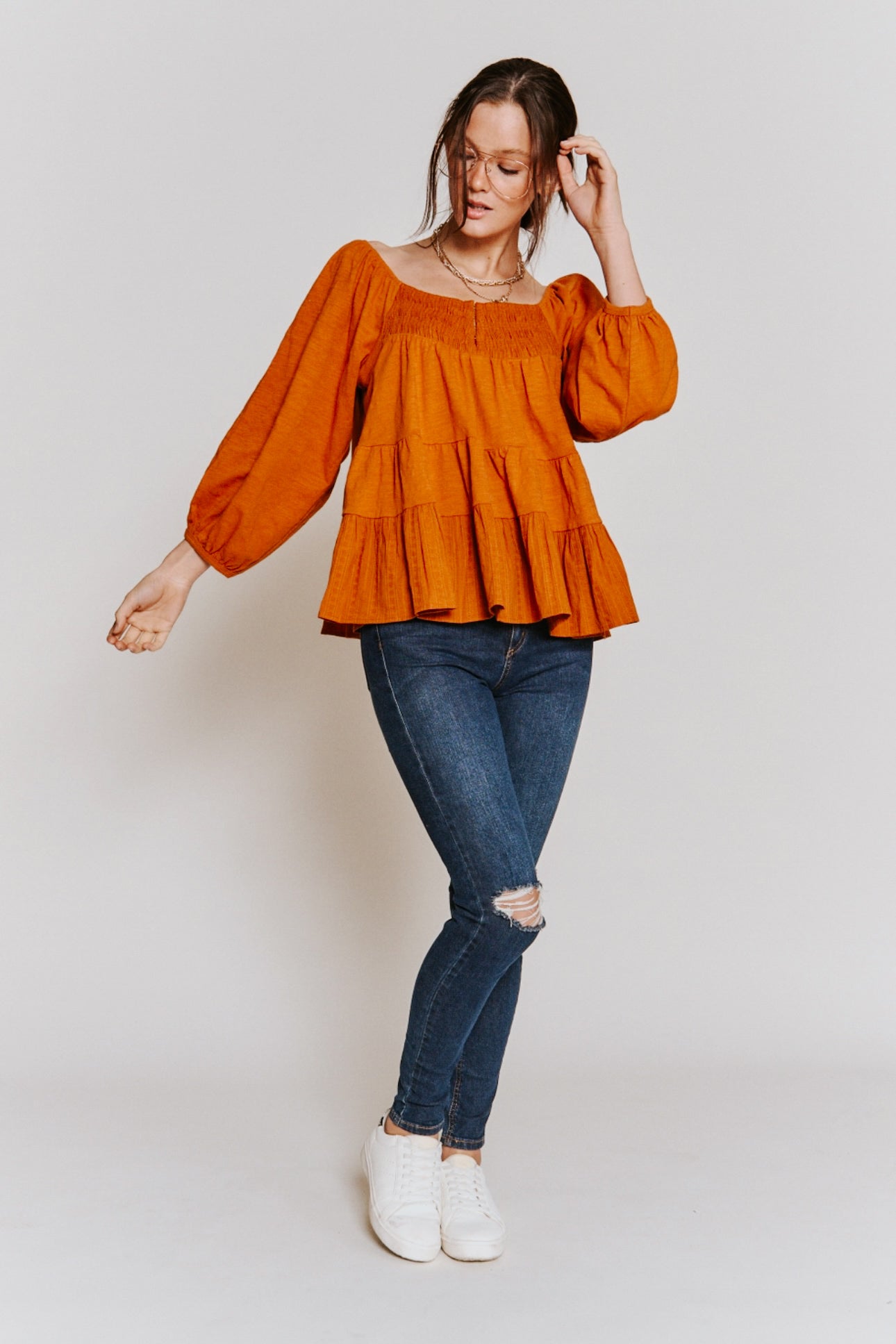 Woman wearing rust ruched babydoll top with puff sleeves paired with ripped dark skinny jeans and white sneakers