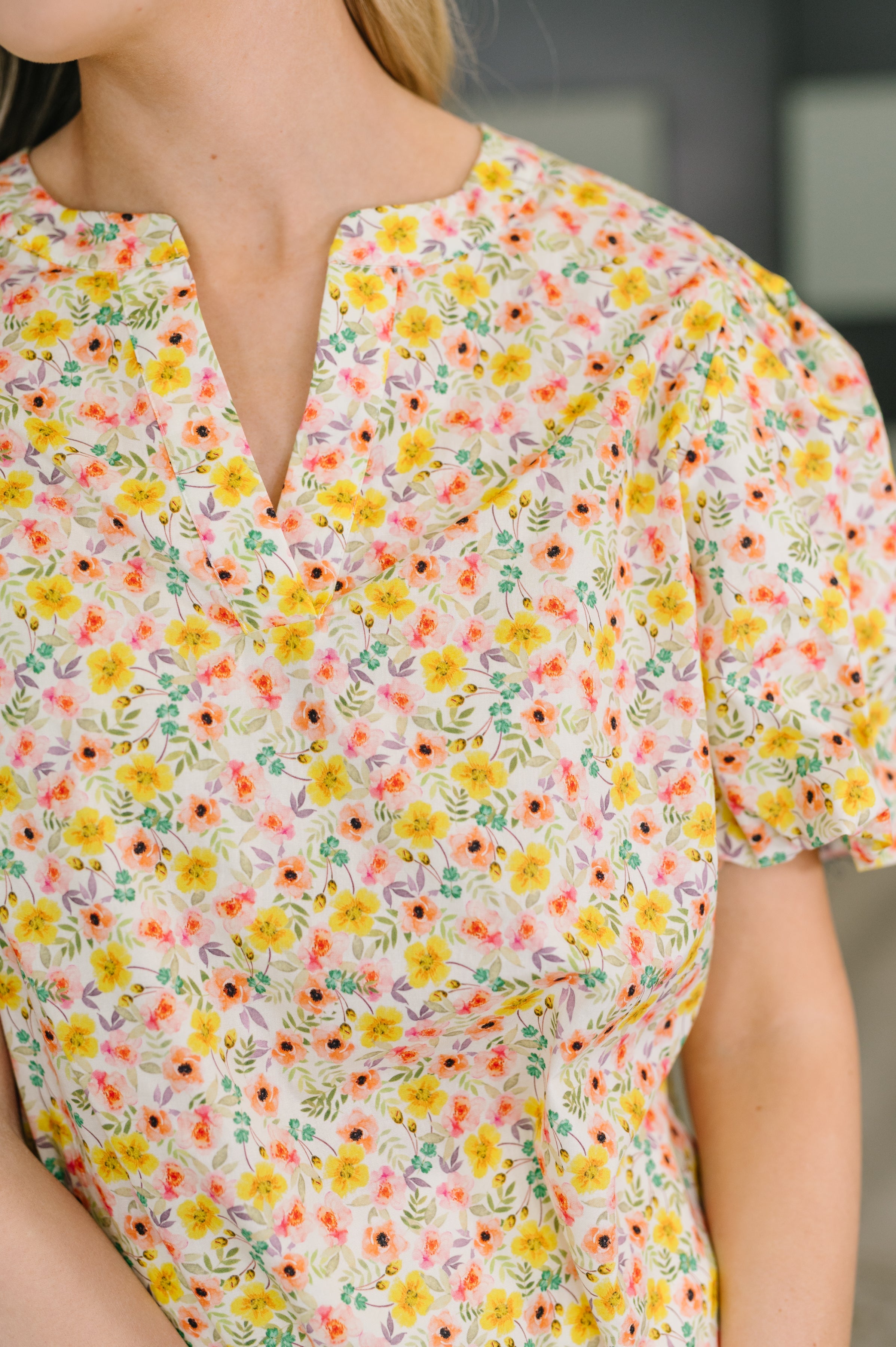 Close-up of woman wearing a yellow floral blouse with balloon sleeves and a notched neckline in soft lighting