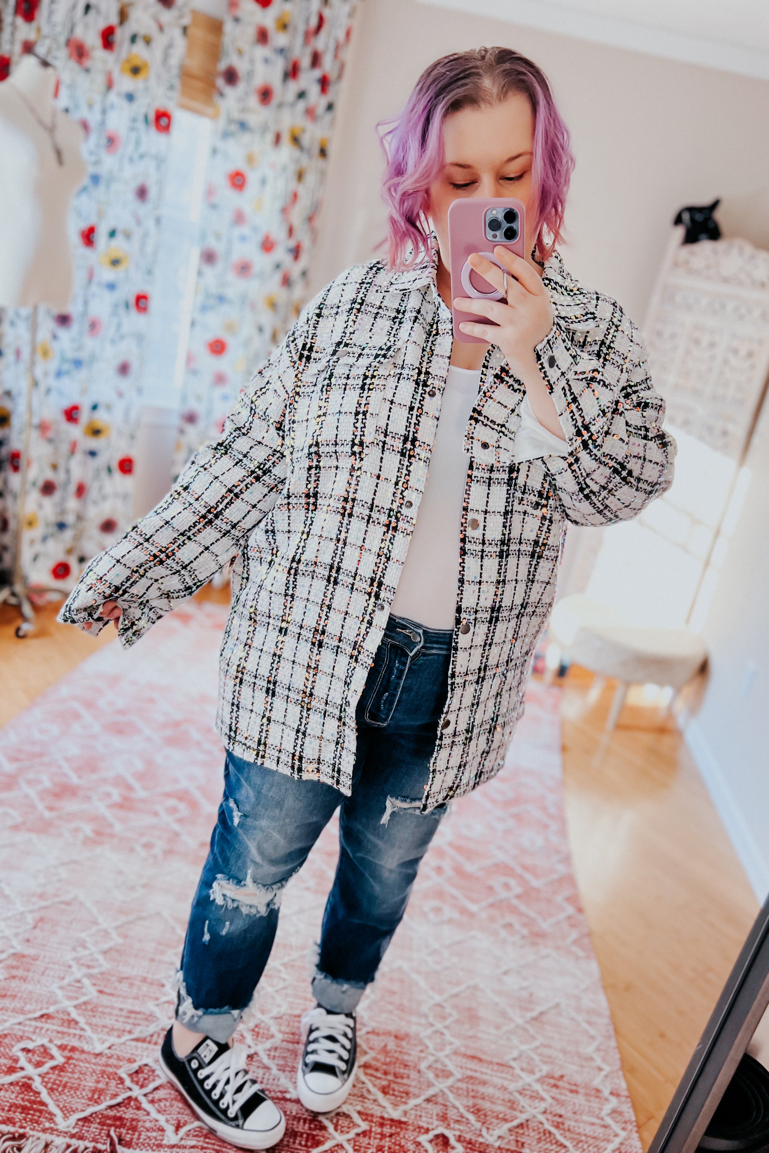 Woman with purple hair wearing white sequin plaid shacket over white top with distressed blue jeans and black sneakers taking selfie