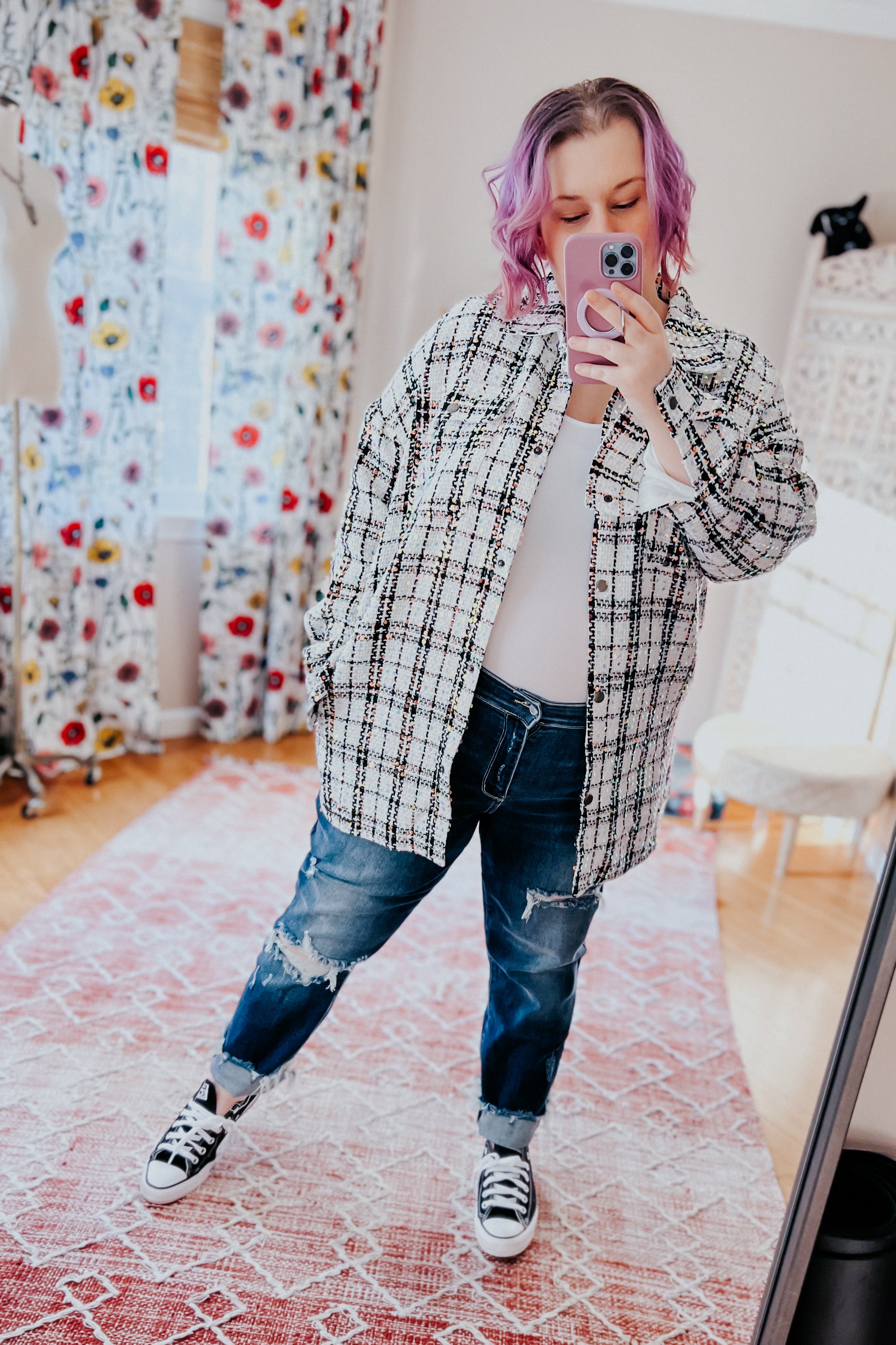 Woman with purple hair wearing white sequin plaid shacket over white top paired with ripped blue jeans and black sneakers taking selfie