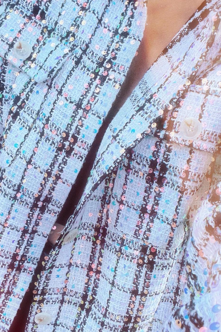 Close-up of white plaid shacket with sequins and textured fabric featuring buttons and pockets in soft lighting