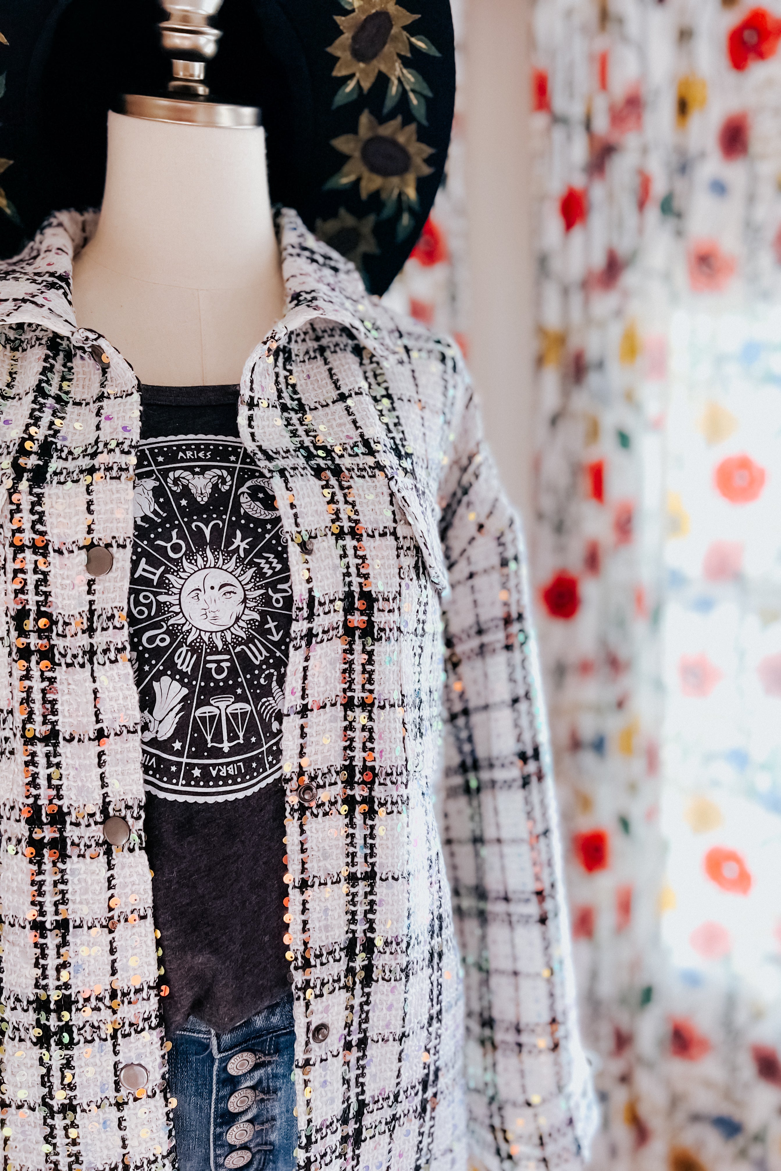 White sequin plaid shacket layered over black zodiac print shirt on mannequin with floral curtain background