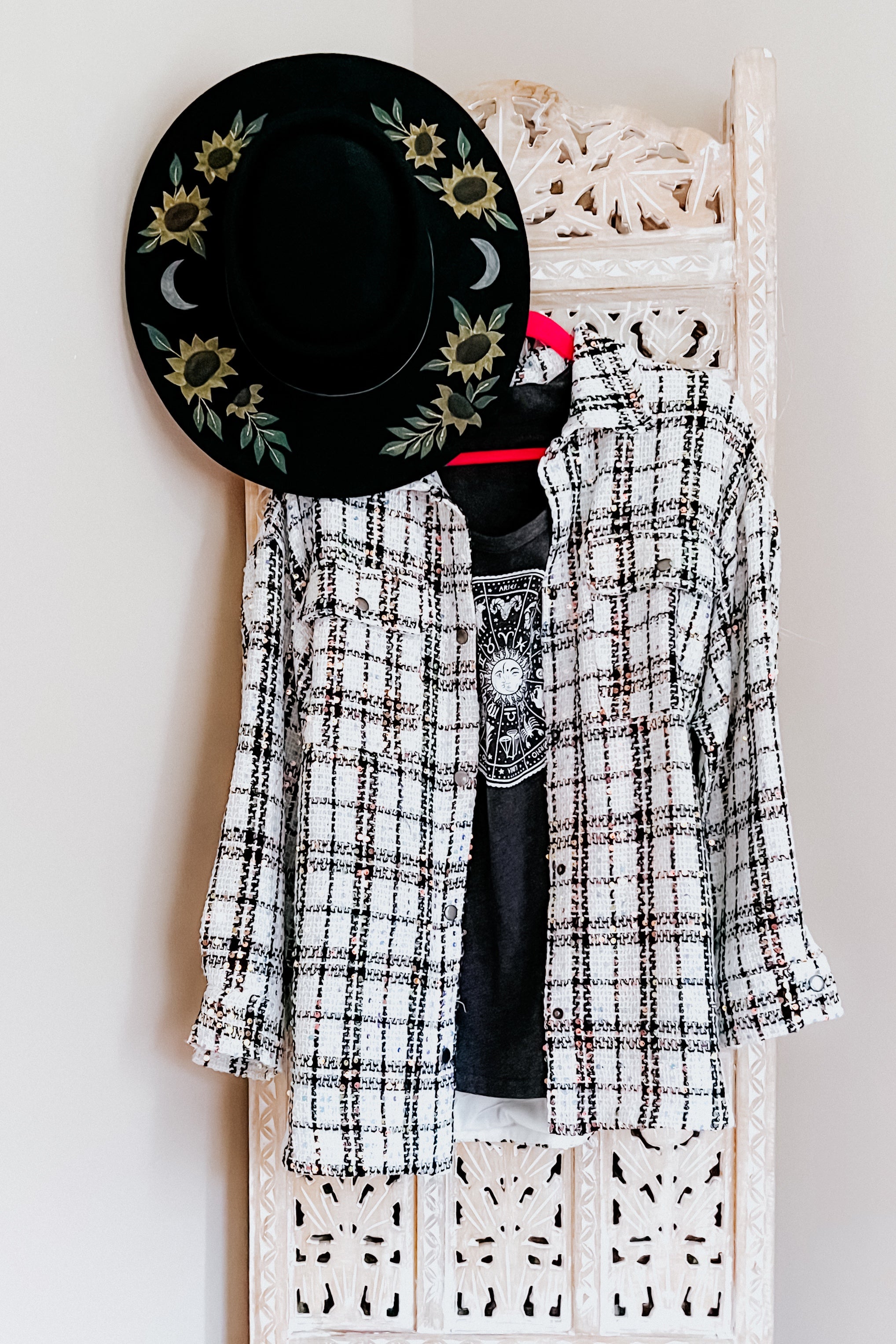 White plaid sequin shacket layered over a black graphic tee, paired with black hat featuring sunflowers and crescent moons