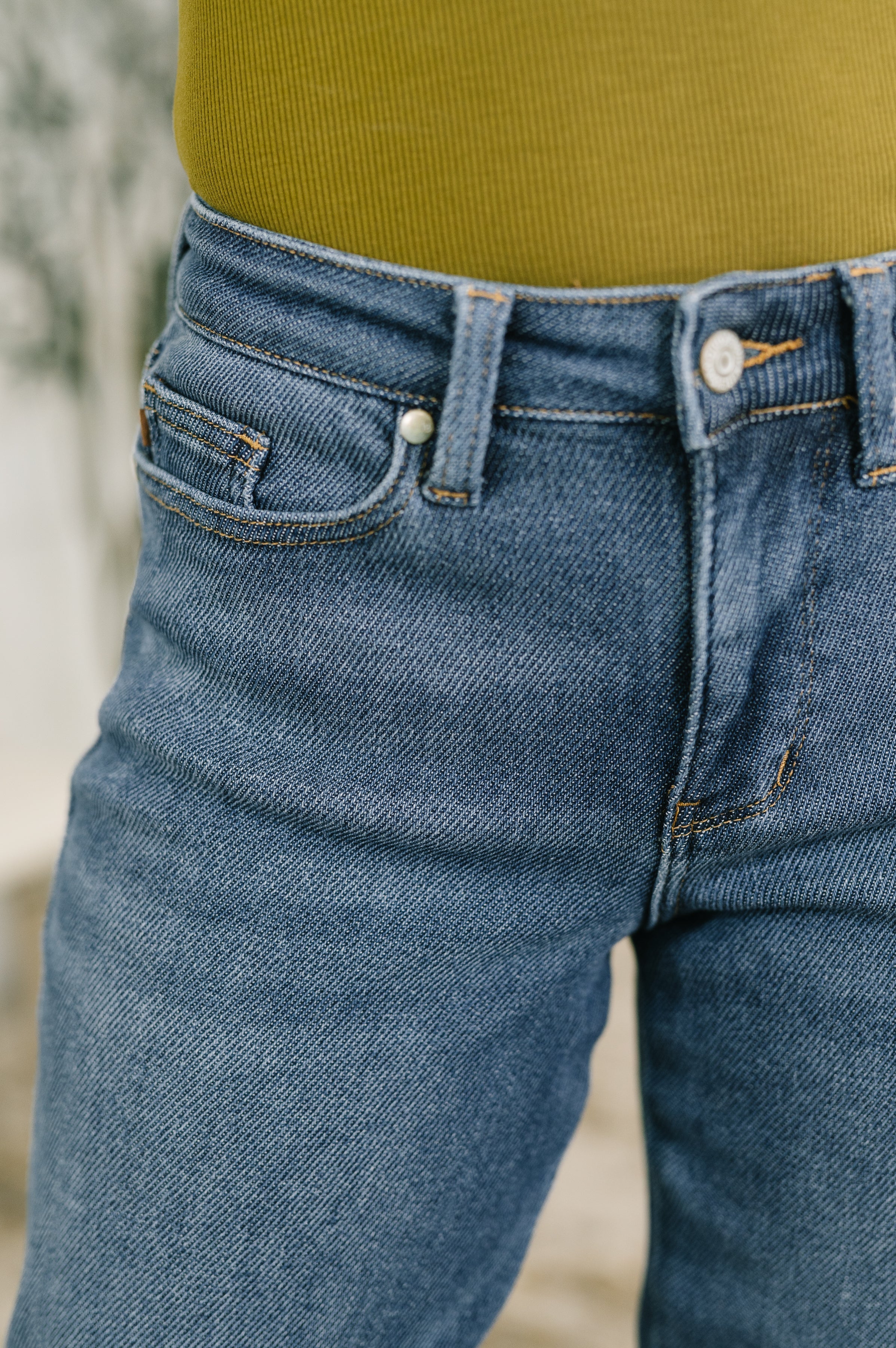 Close-up of mid-rise blue denim boyfriend jeans with relaxed fit and slight fading detail on thigh area