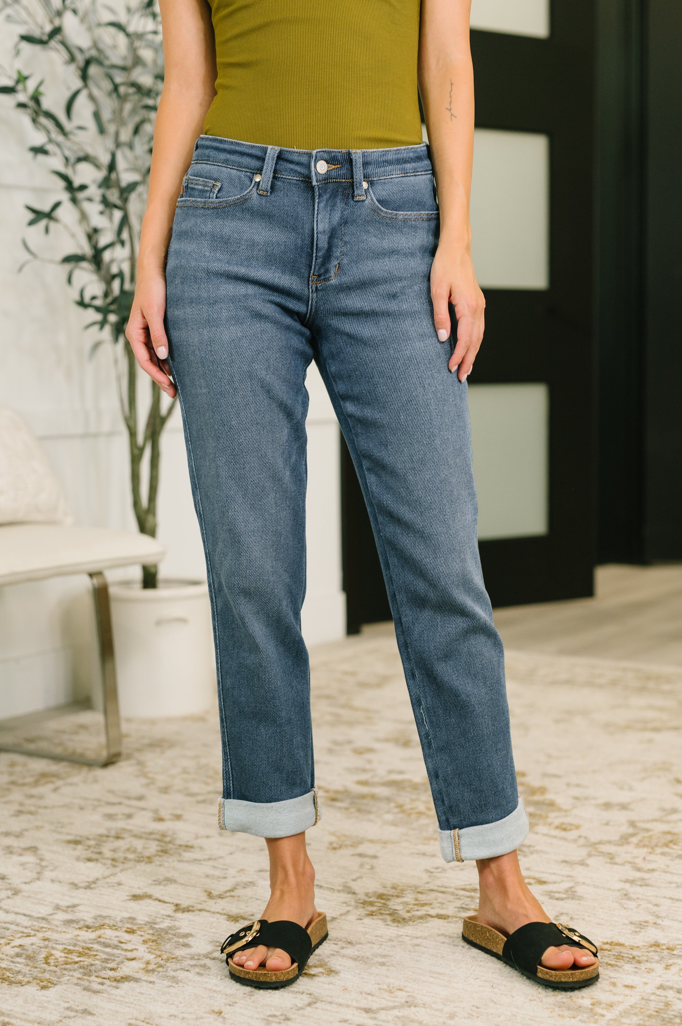 Front view of person wearing mid rise relaxed fit blue denim jeans with cuffed hems and black slide sandals indoors