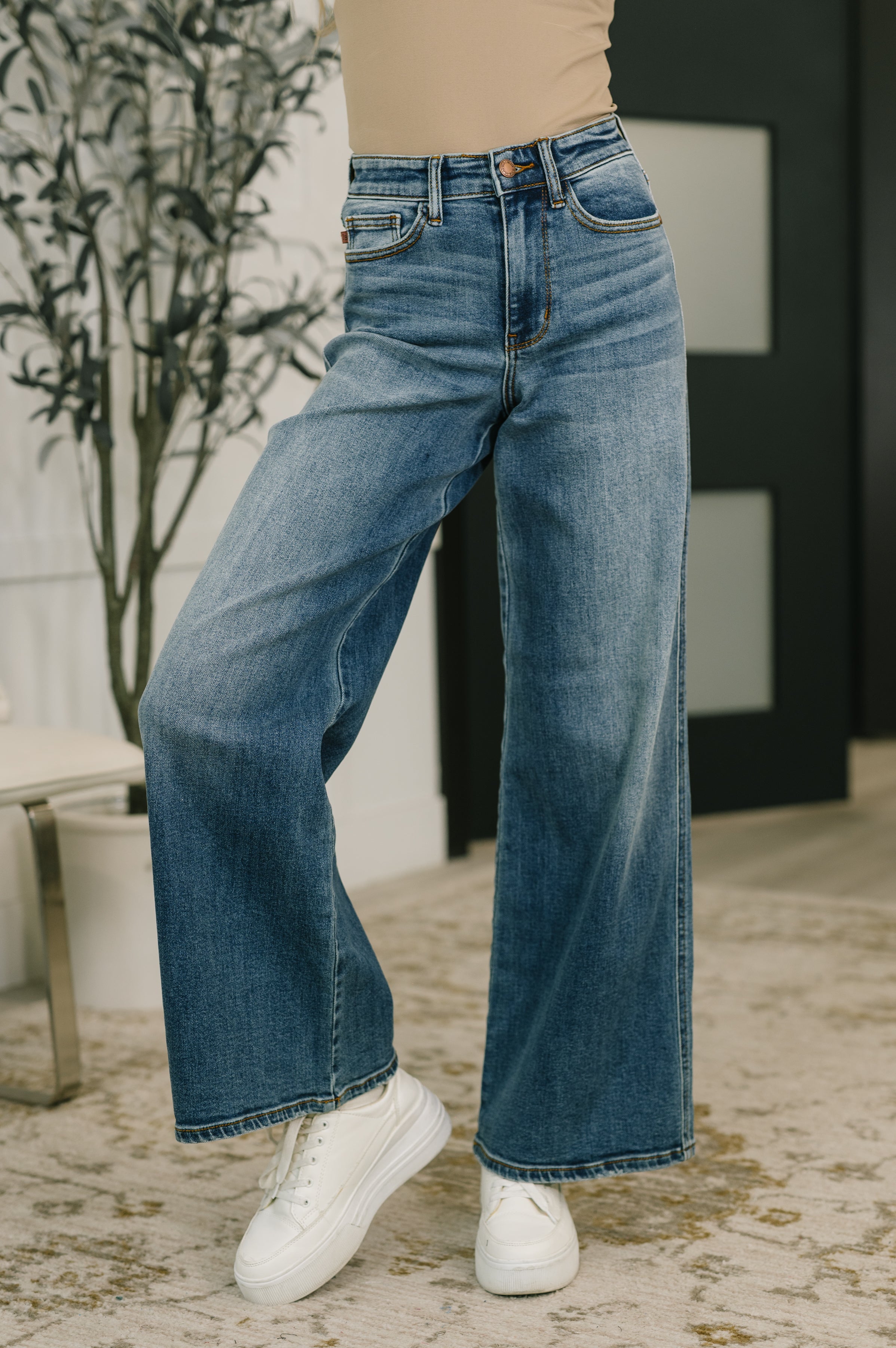 Close-up of high waist blue wide-leg jeans paired with white platform sneakers indoors on patterned rug