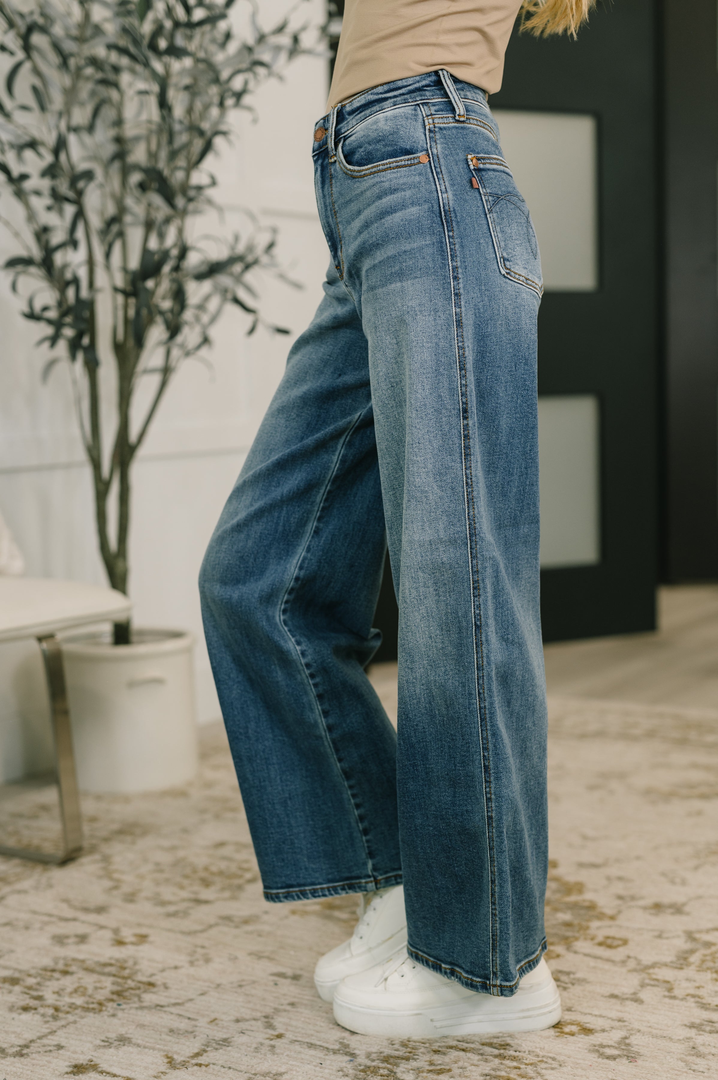 Side view of blue high waist wide leg jeans paired with white sneakers in indoor setting