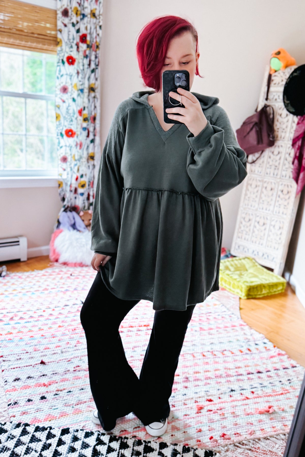 Woman taking a mirror selfie in a teal hooded V neck pullover with balloon sleeves and gathered waist, styled with black leggings and sneakers in a bedroom