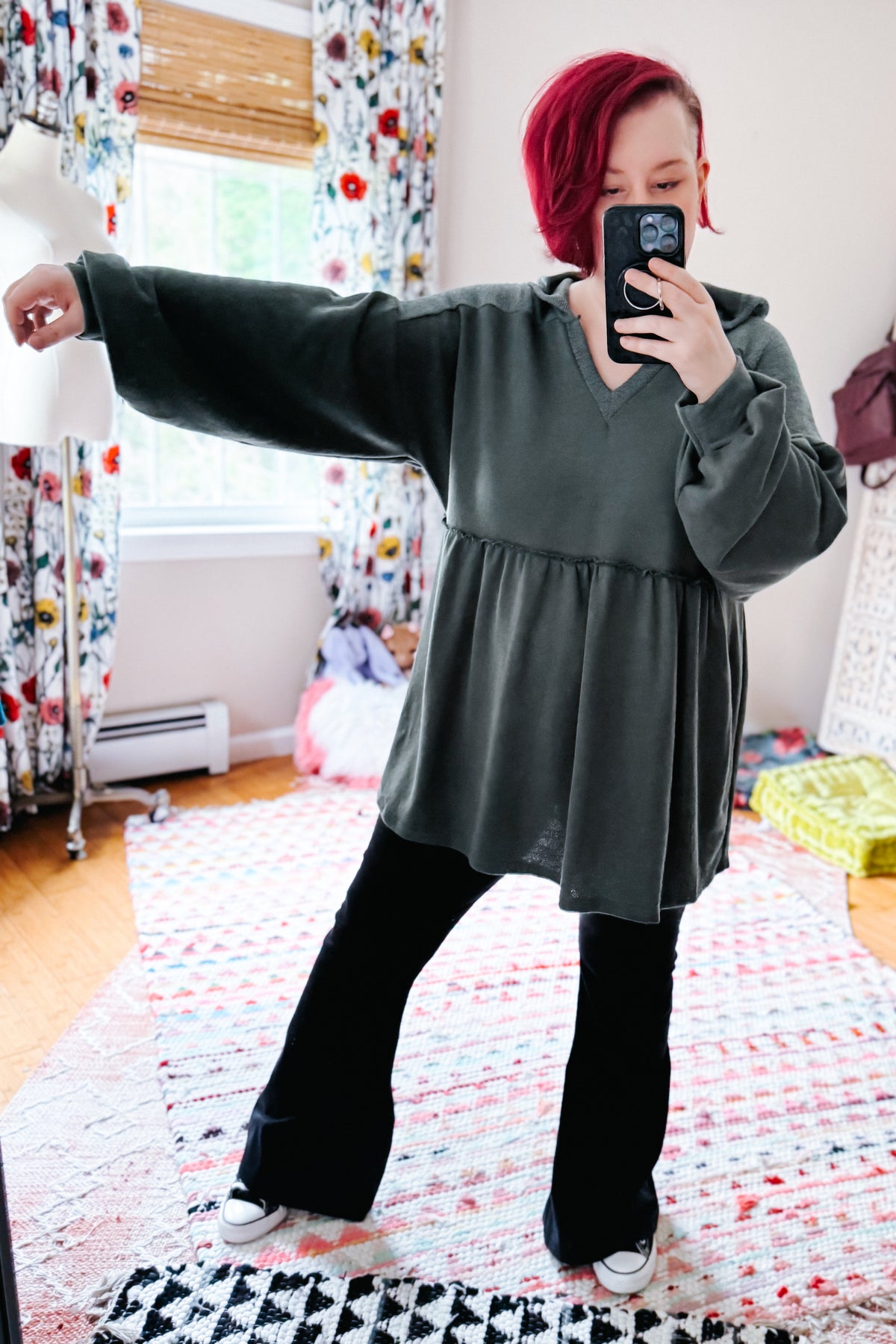 Woman taking a mirror selfie in a teal hooded V-neck pullover with gathered peplum and balloon sleeves over black pants