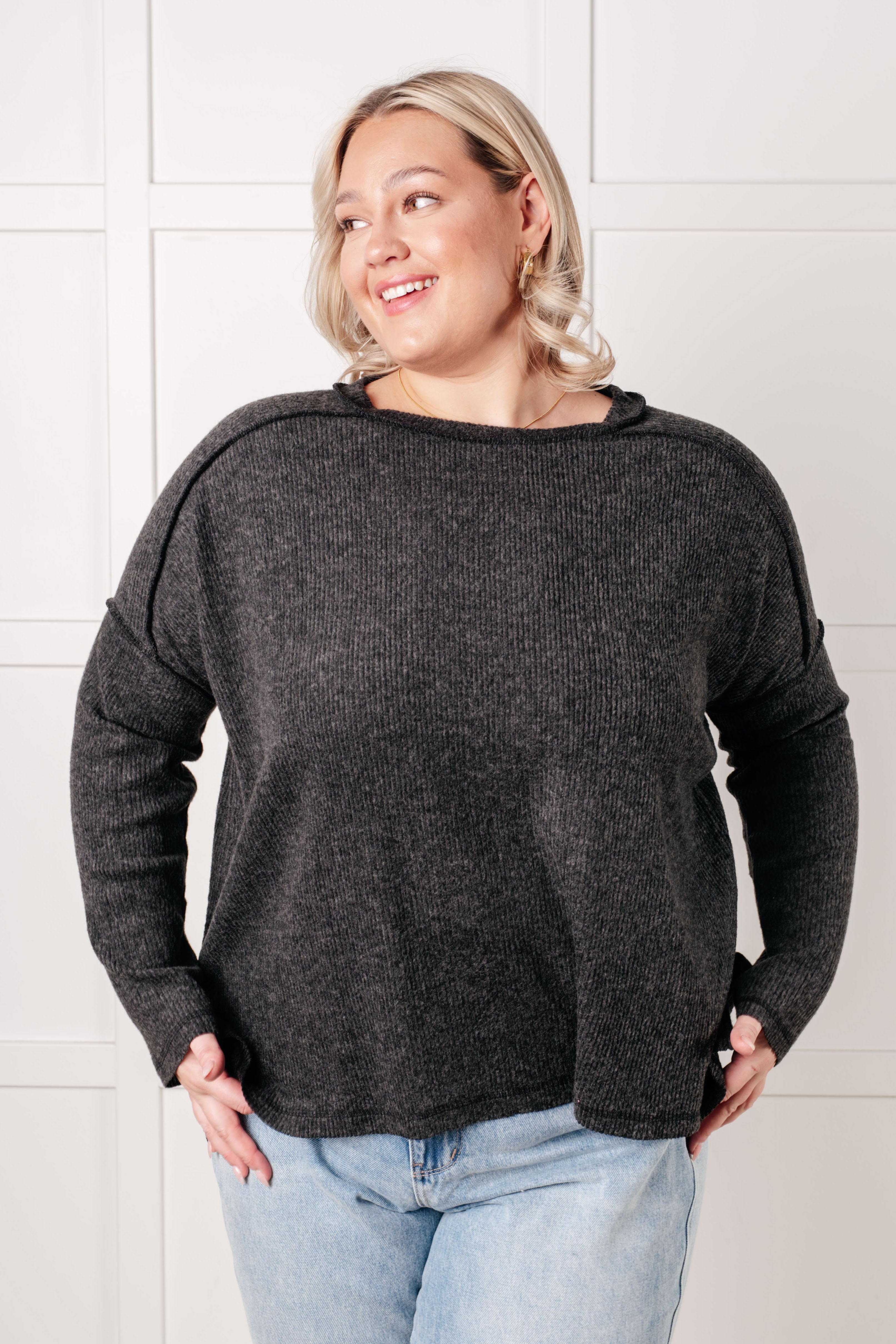 Smiling woman wearing cozy black ribbed sweater with relaxed fit and long sleeves paired with light blue jeans