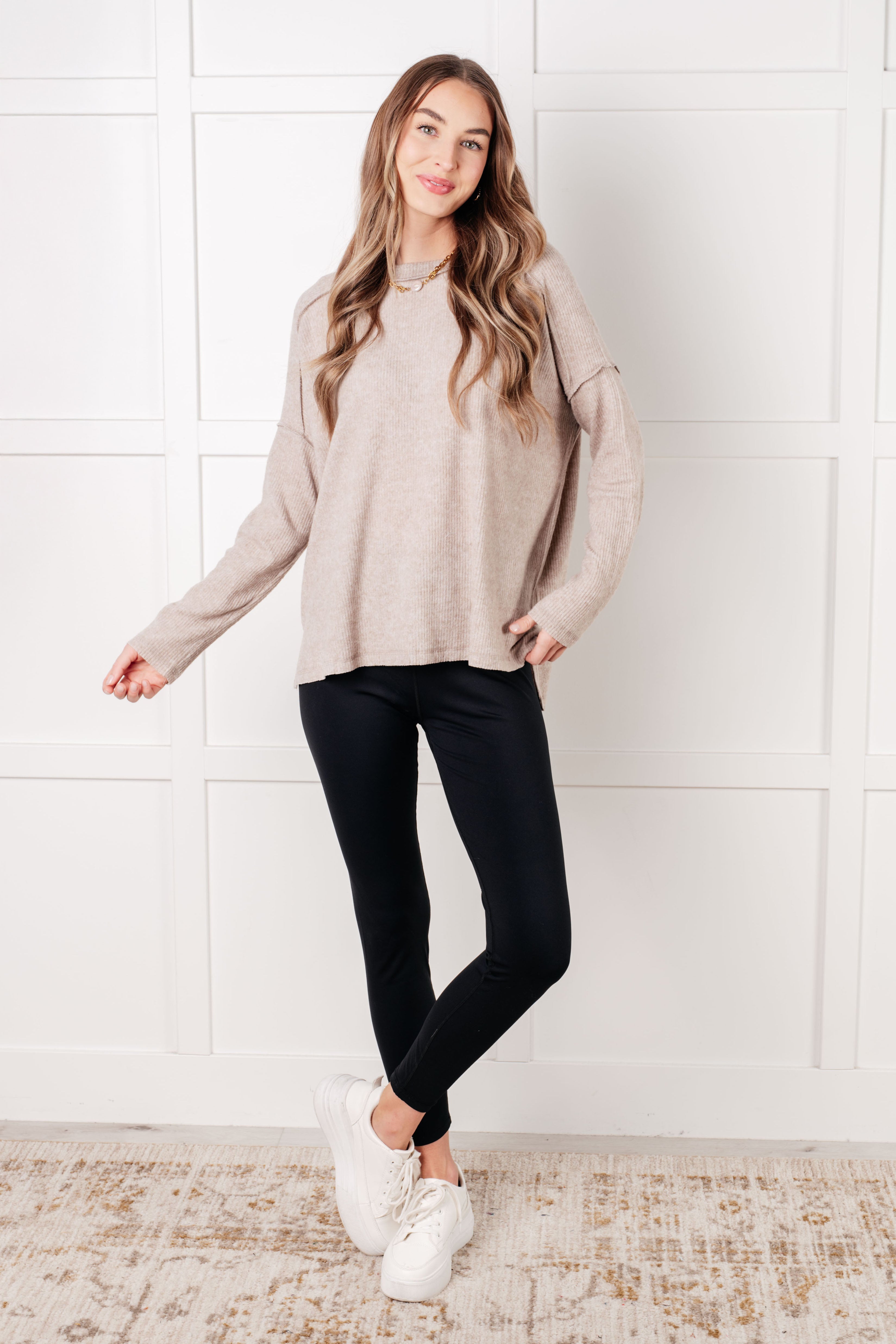 Woman wearing relaxed heather mocha ribbed sweater with black leggings and white sneakers in bright indoor setting