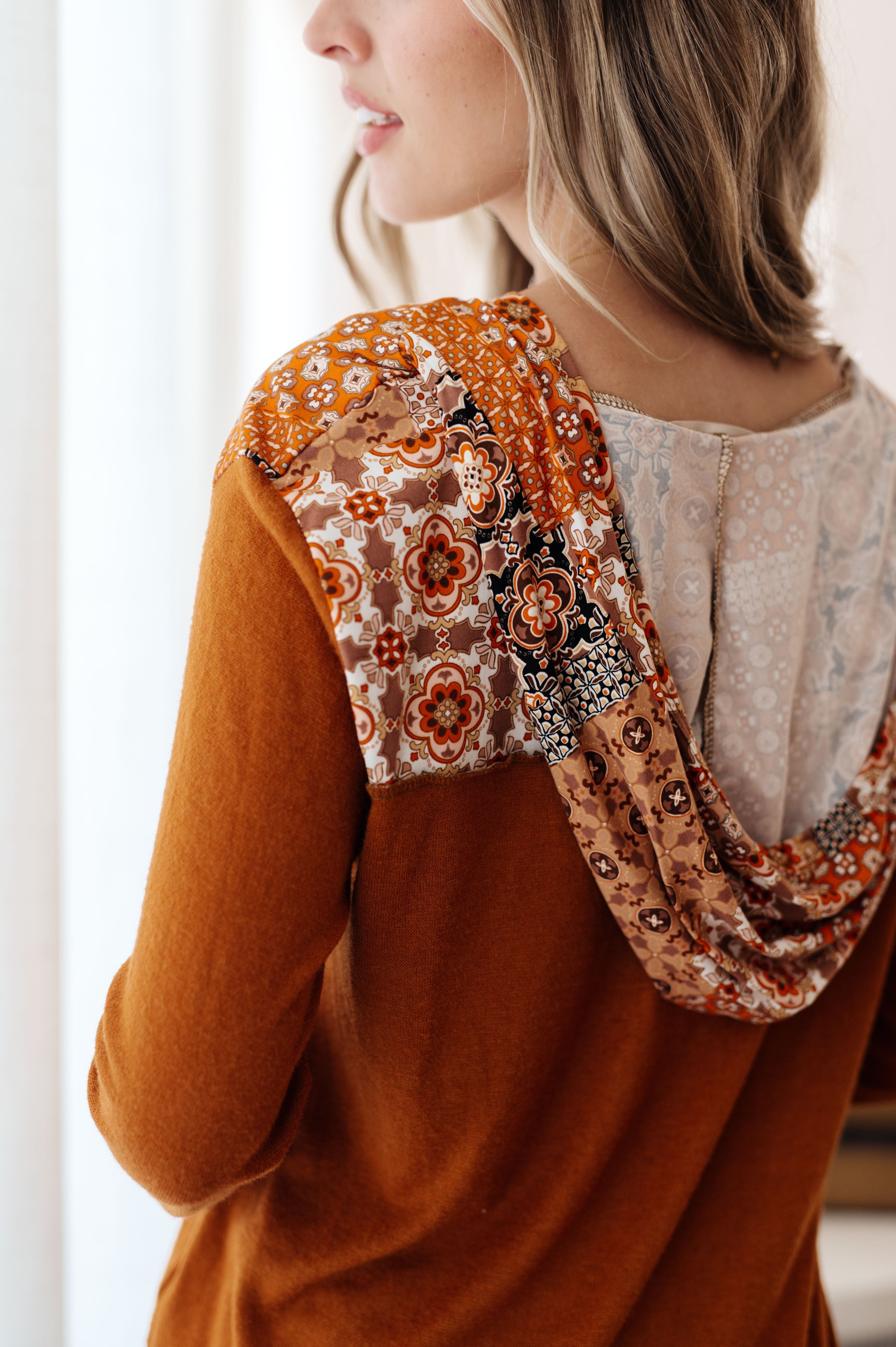 Woman shown from behind wearing rust-colored hoodie with mixed print floral patchwork on hood and shoulders
