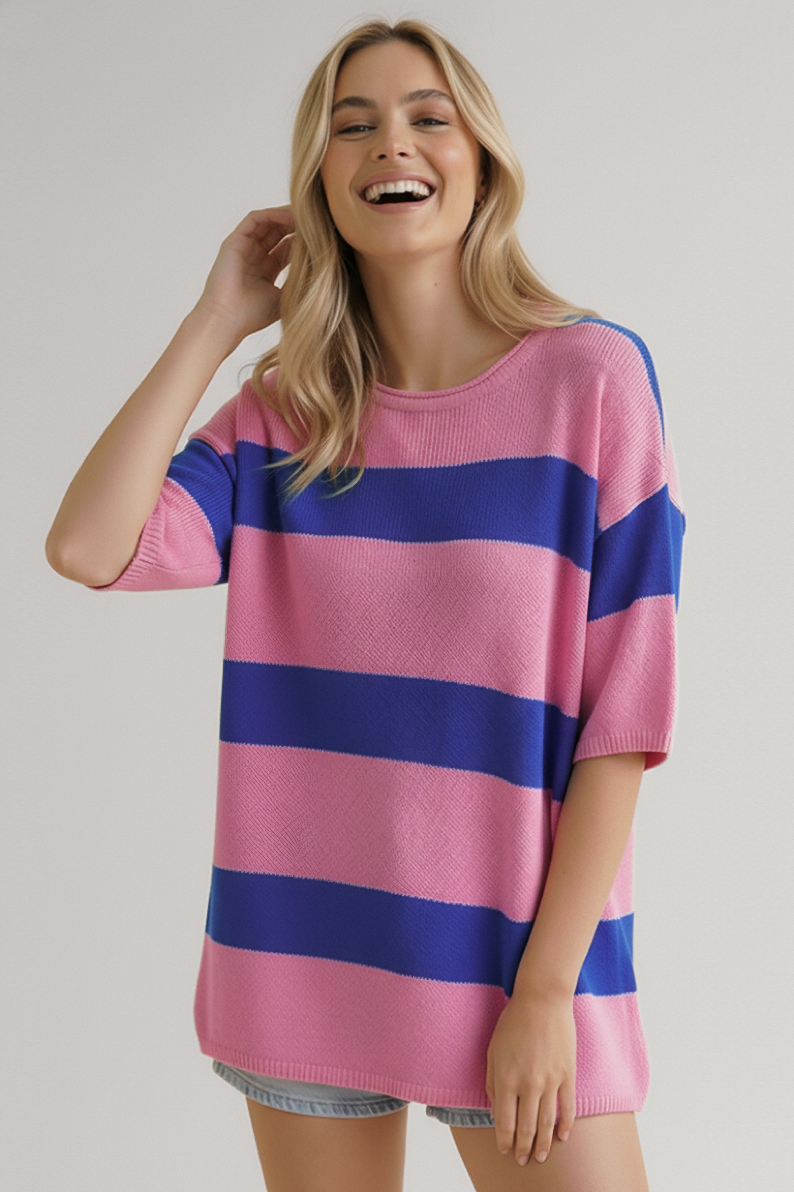 Smiling woman wearing a casual pink and blue striped knit top with short sleeves and light denim shorts