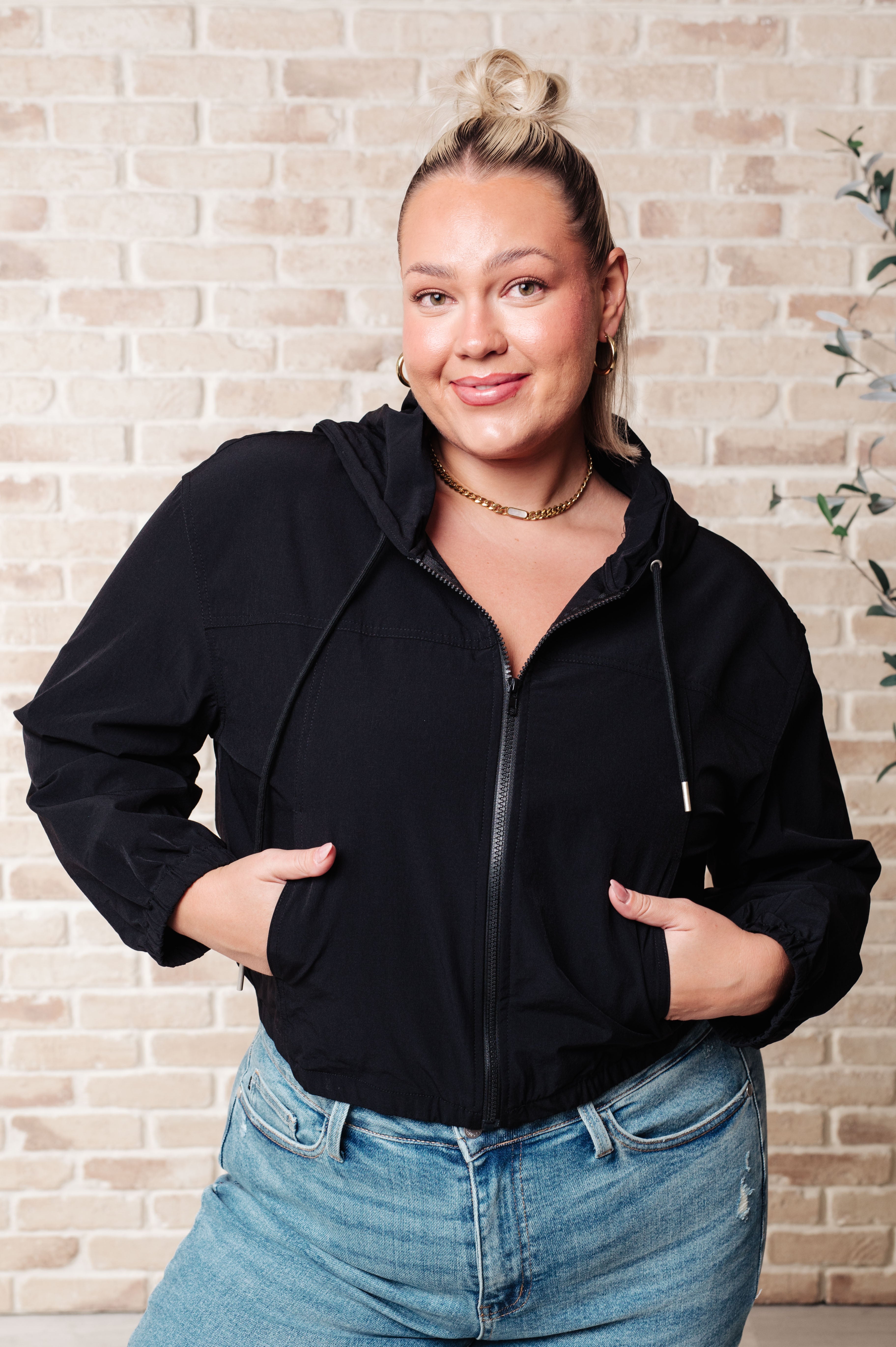 Plus-size woman wearing black zip-up hoodie with hood and drawstrings paired with light wash jeans and gold necklace