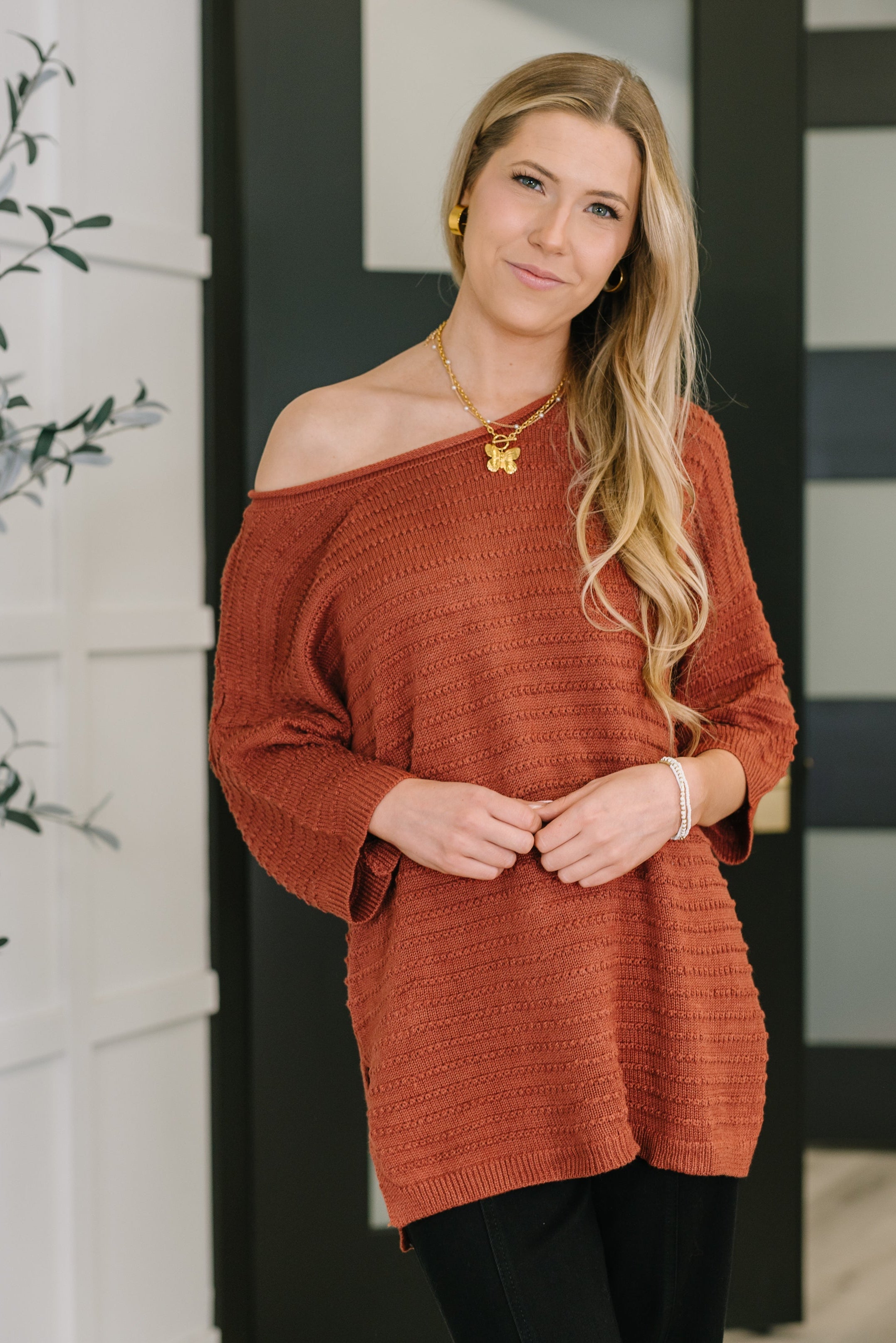 Woman wearing marsala textured off shoulder top paired with black pants standing indoors with subtle smile