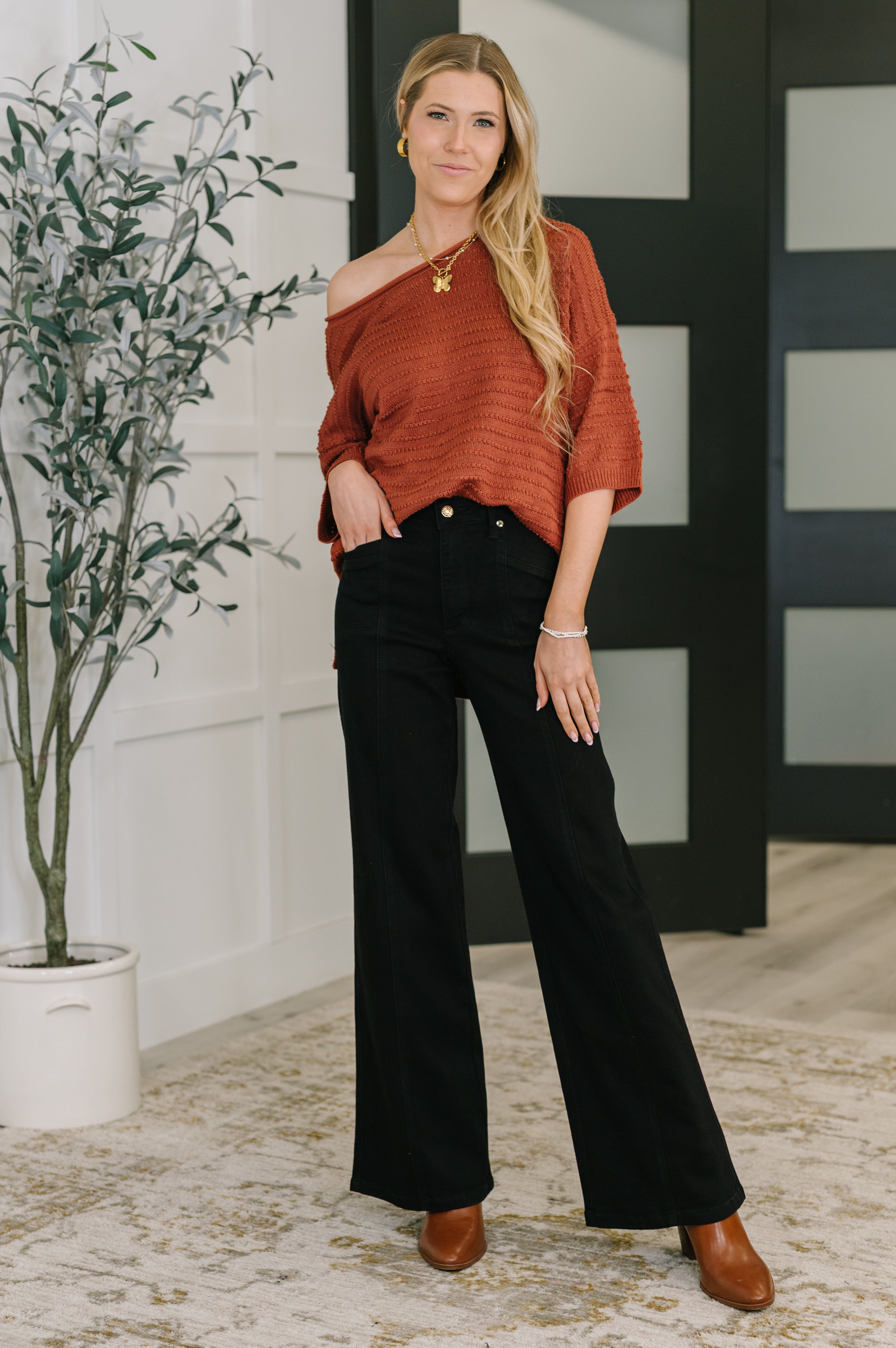 Woman wearing marsala off shoulder textured top paired with black wide-leg pants and brown ankle boots indoors
