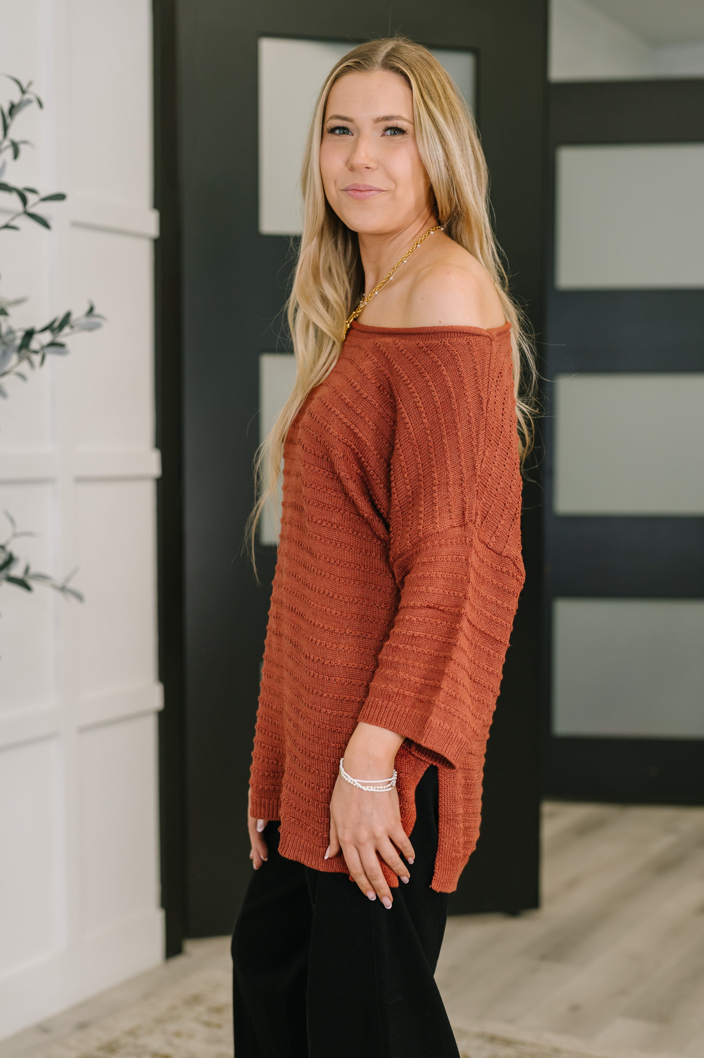 Woman wearing marsala off shoulder textured top with long sleeves standing indoors by black door