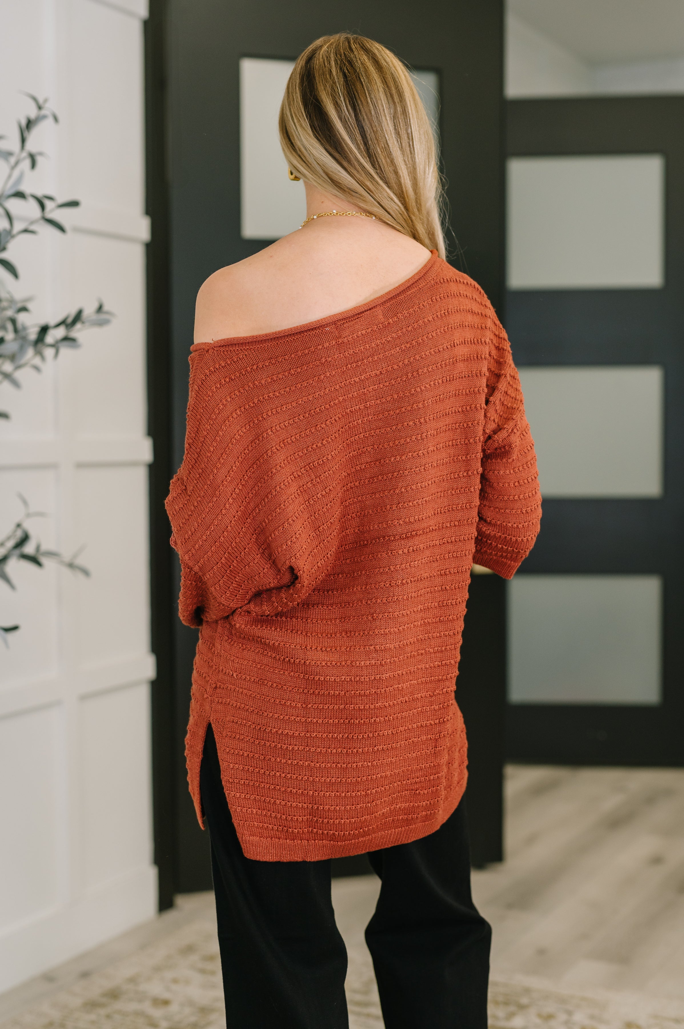 Back view of Marsala textured off-shoulder top with slouchy fit worn with black pants in modern room