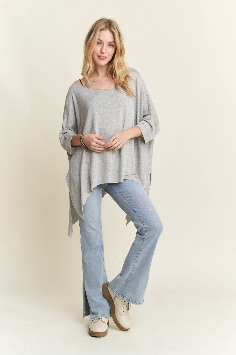 Woman wearing loose grey flowy top with raw edges paired with light blue split hem jeans and beige shoes
