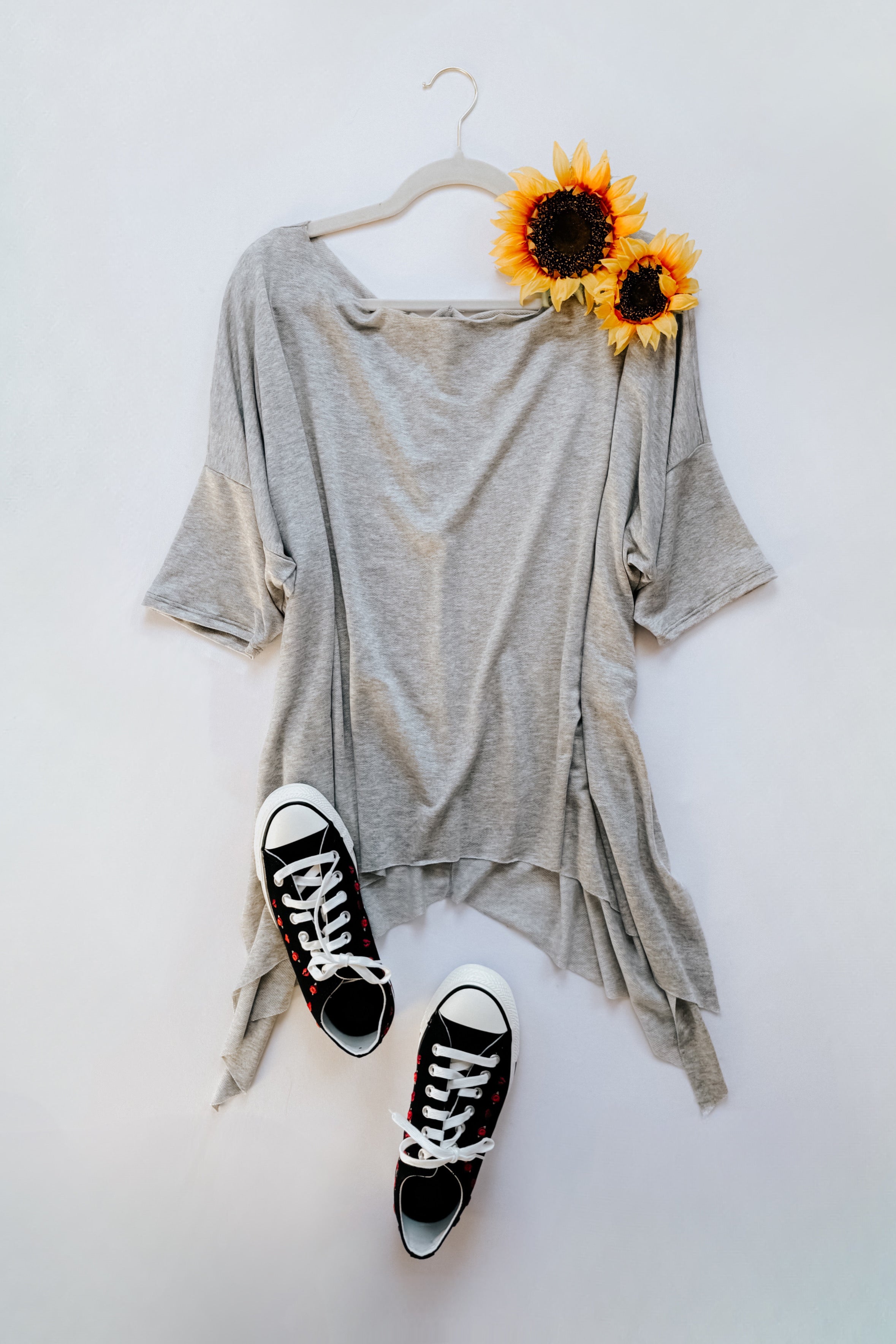 Grey flowy top with raw edge shark-bite hem paired with black high-top sneakers and two sunflowers on hanger