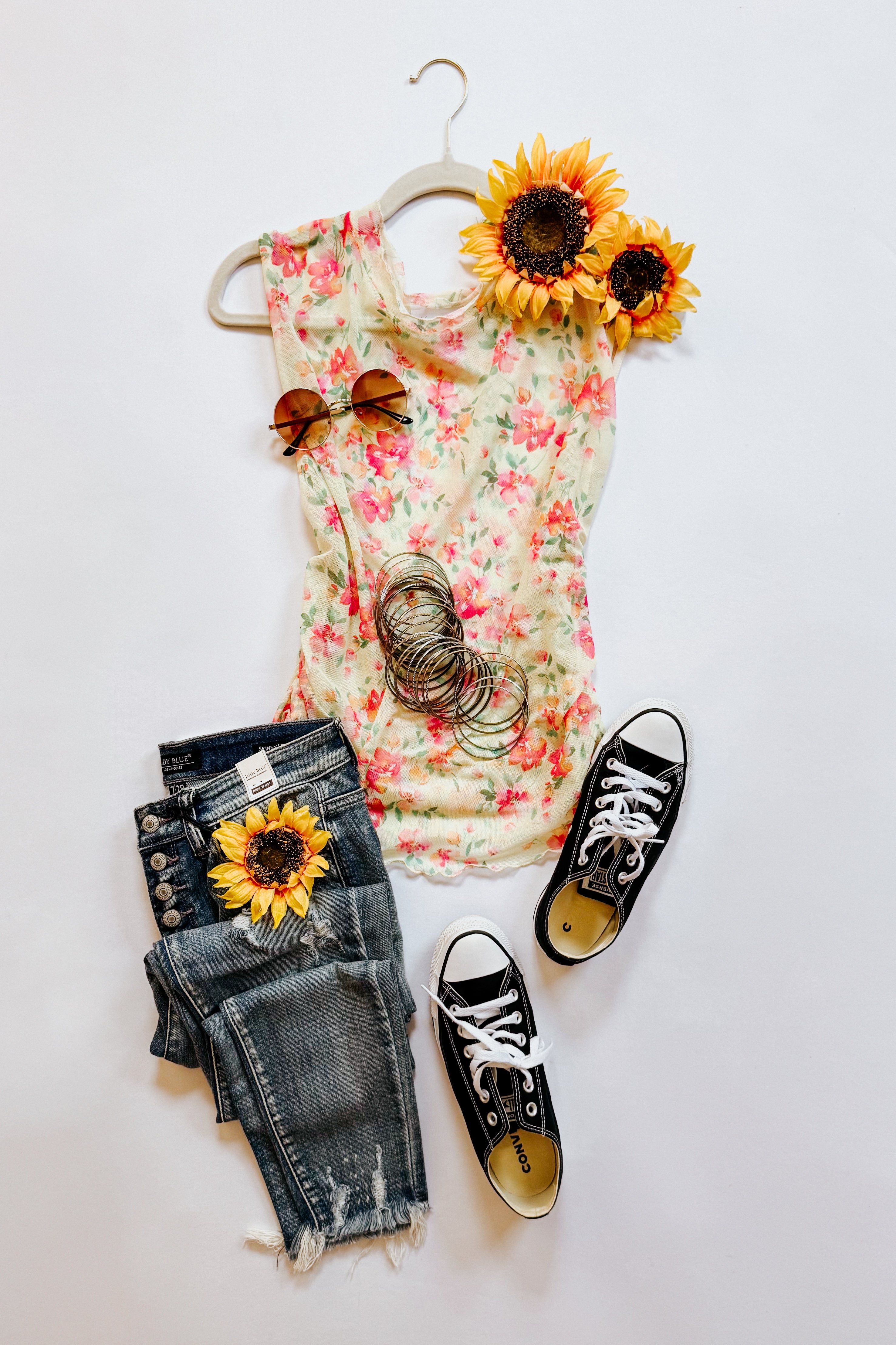 Sleeveless floral top with pink and green print paired with distressed dark denim jeans and black Converse sneakers