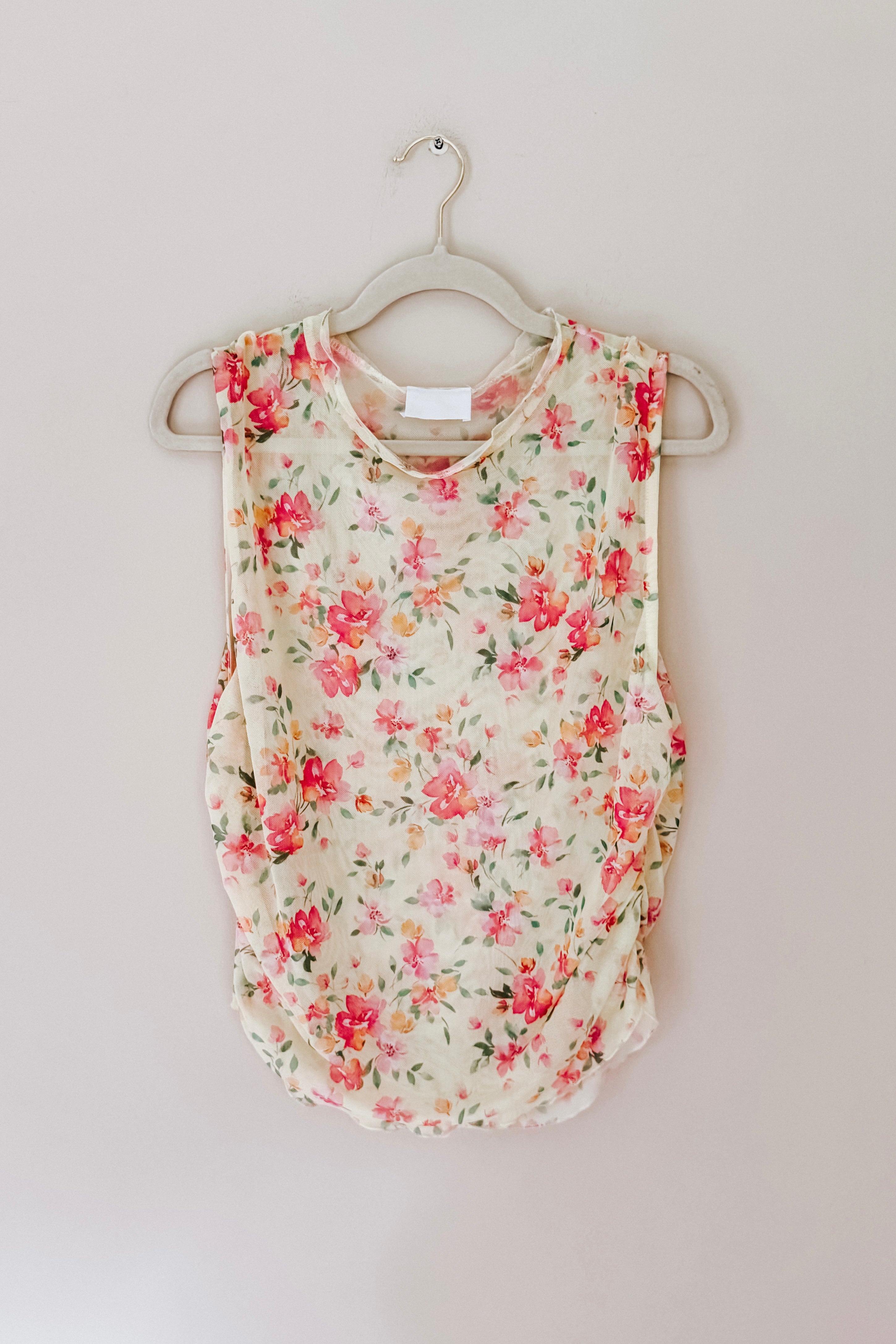 Sleeveless sheer layering top with bright floral print in pink and green tones on cream background