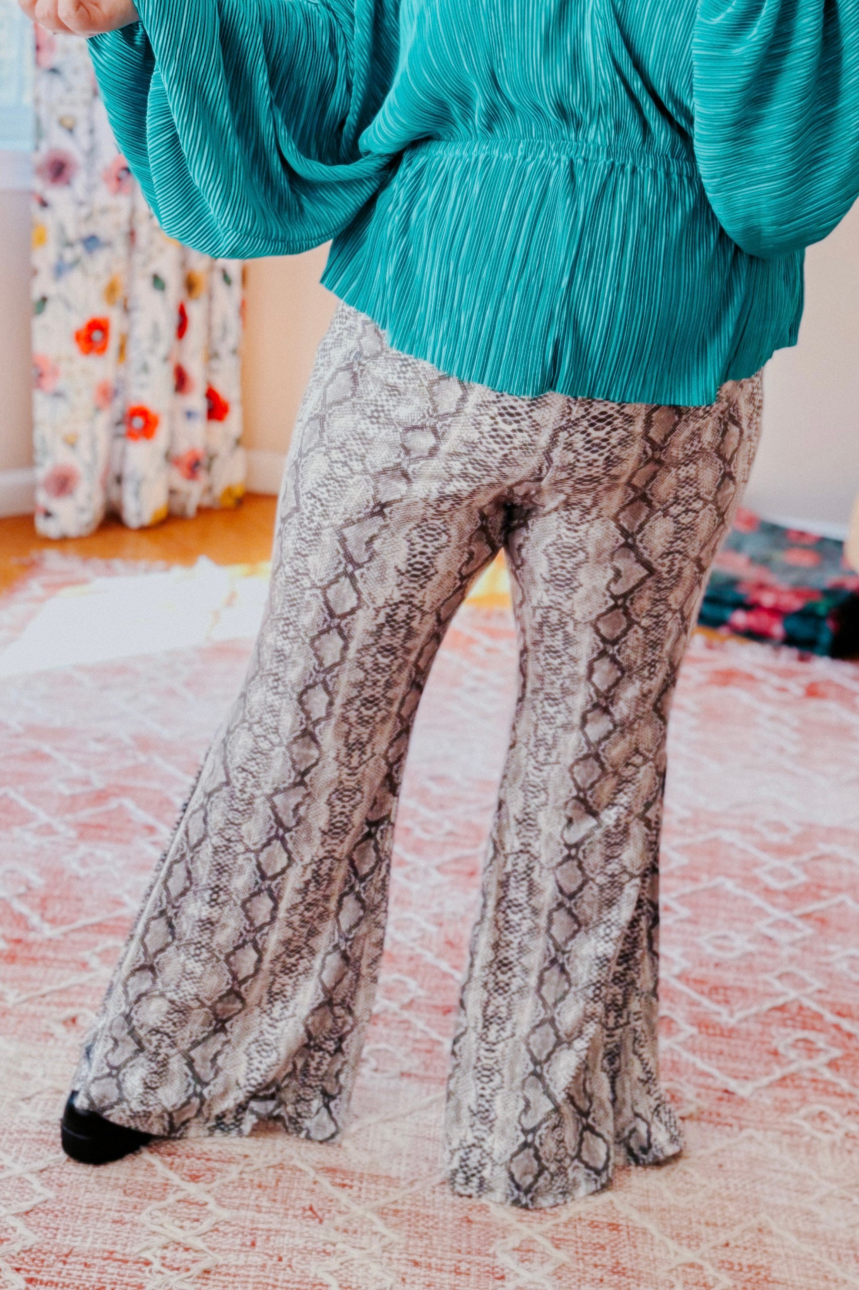 Soft grey snake print flare pants worn with teal textured top indoors on patterned rug