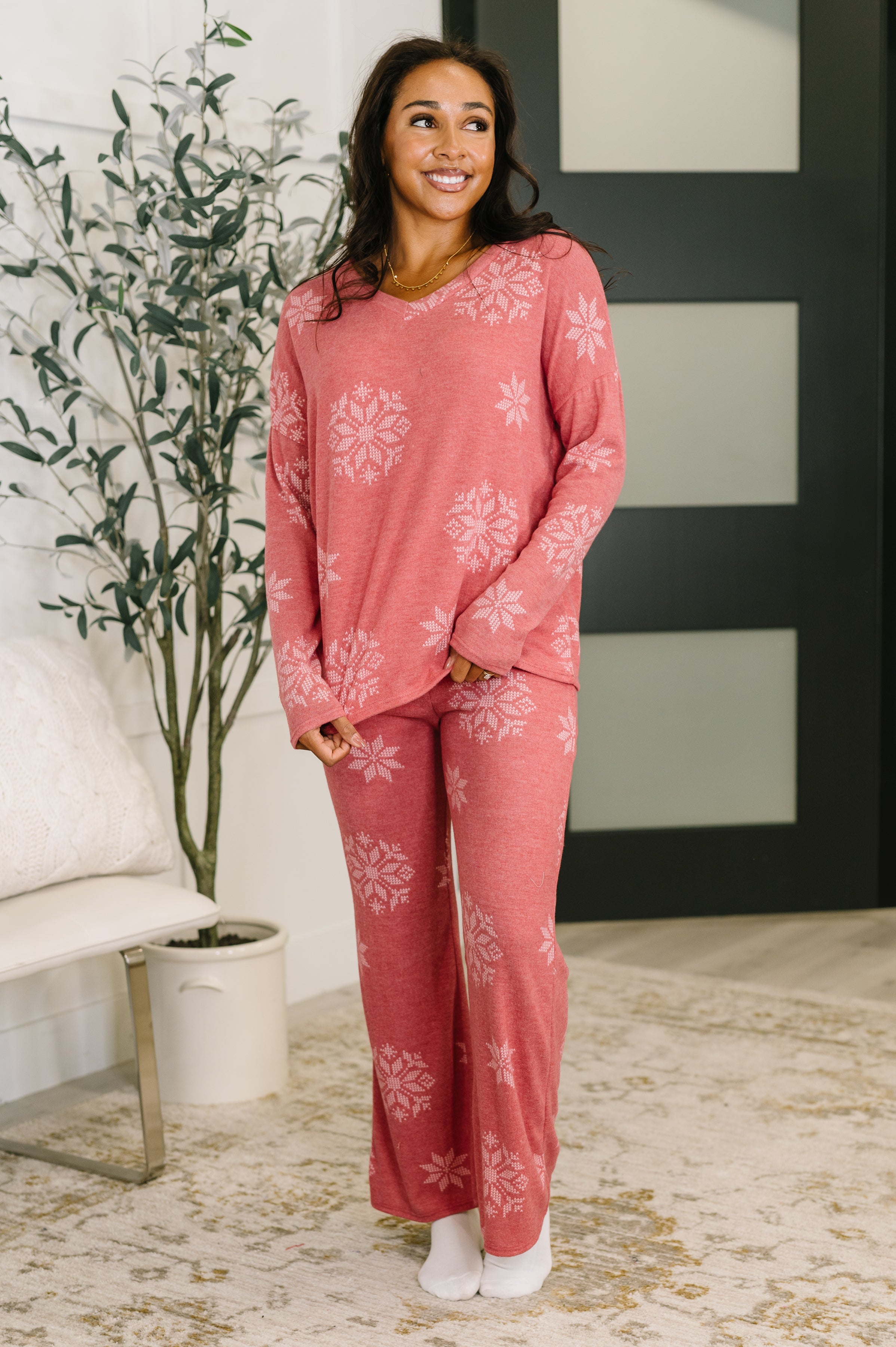 Smiling woman wearing red snowflake patterned cozy pajama set standing indoors near plant and modern door