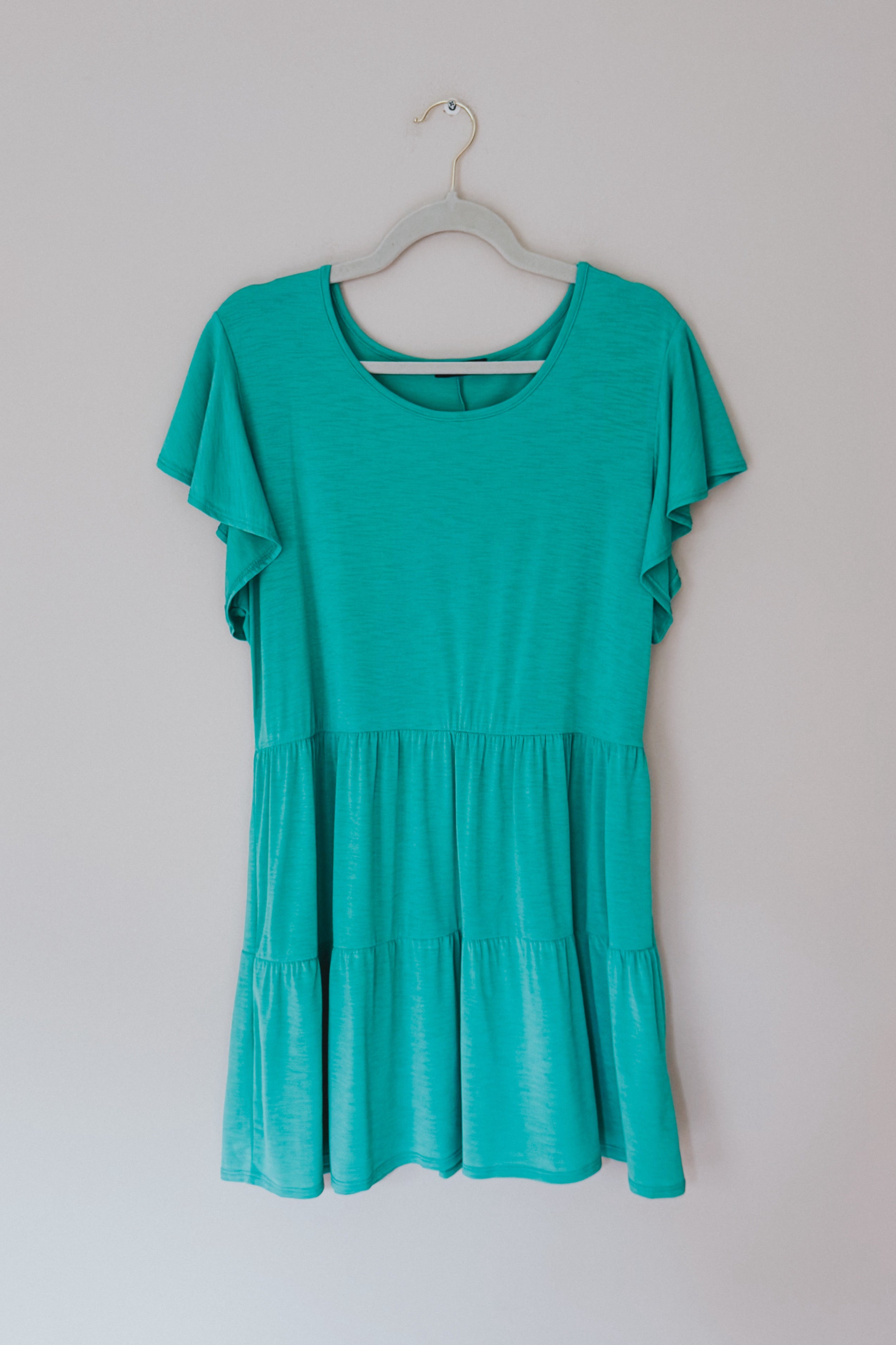Teal short-sleeve babydoll top with tiered ruffle hem hanging on hanger against plain background