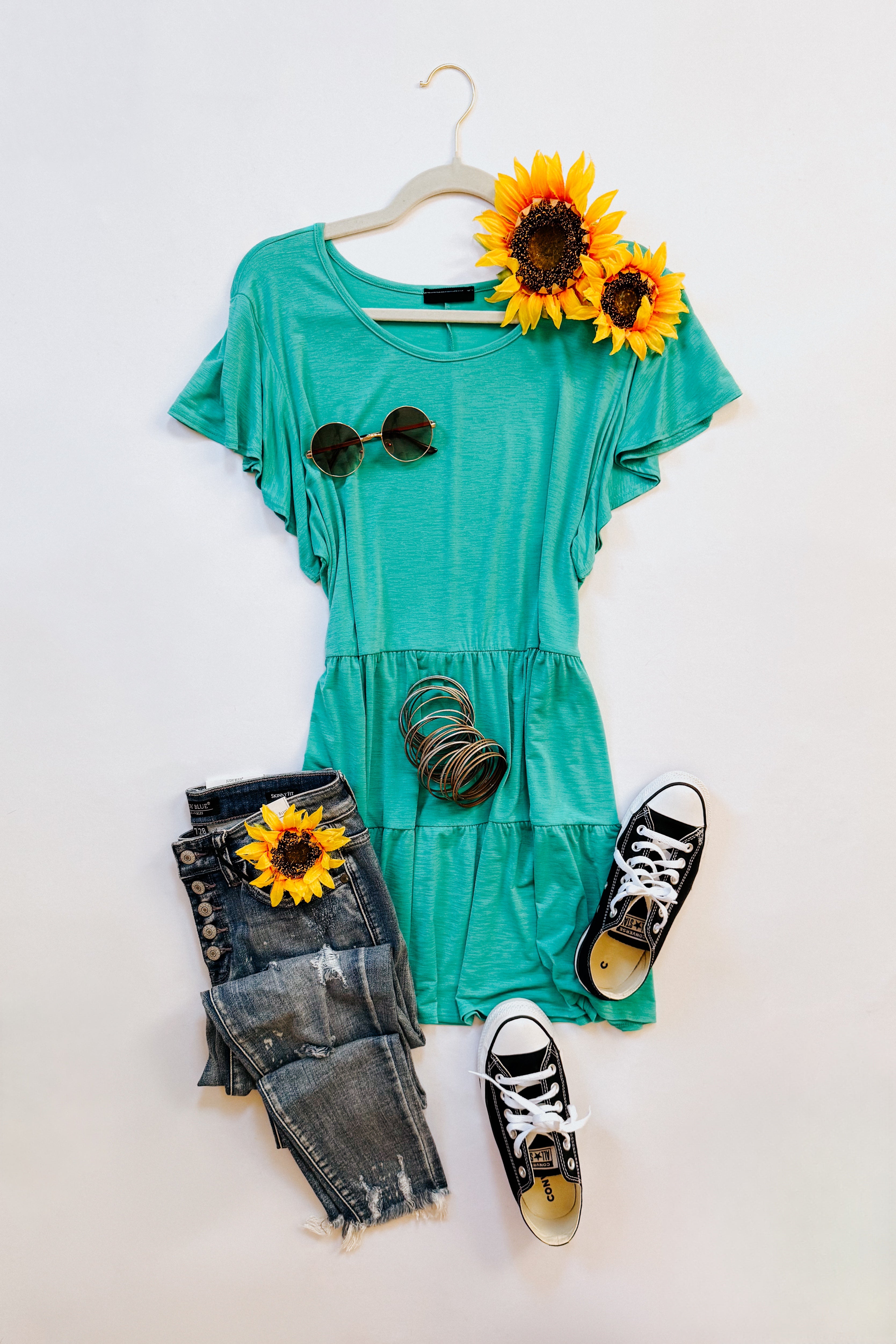 Teal babydoll top with flutter sleeves styled with distressed jeans, black sneakers, sunglasses, bracelets, and sunflowers