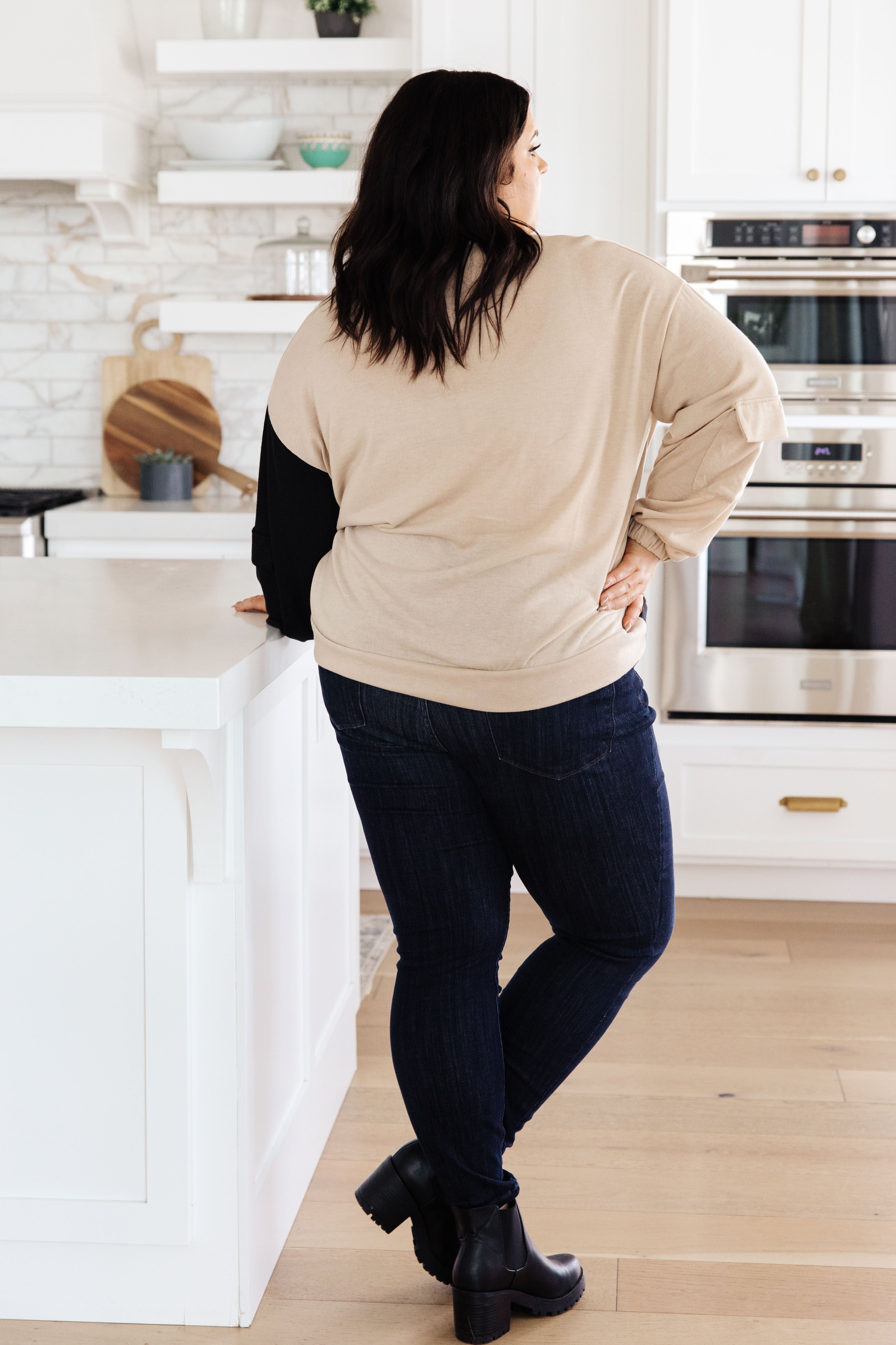 Plus-size woman wearing tan and black color block top with cargo-style sleeves standing in modern kitchen