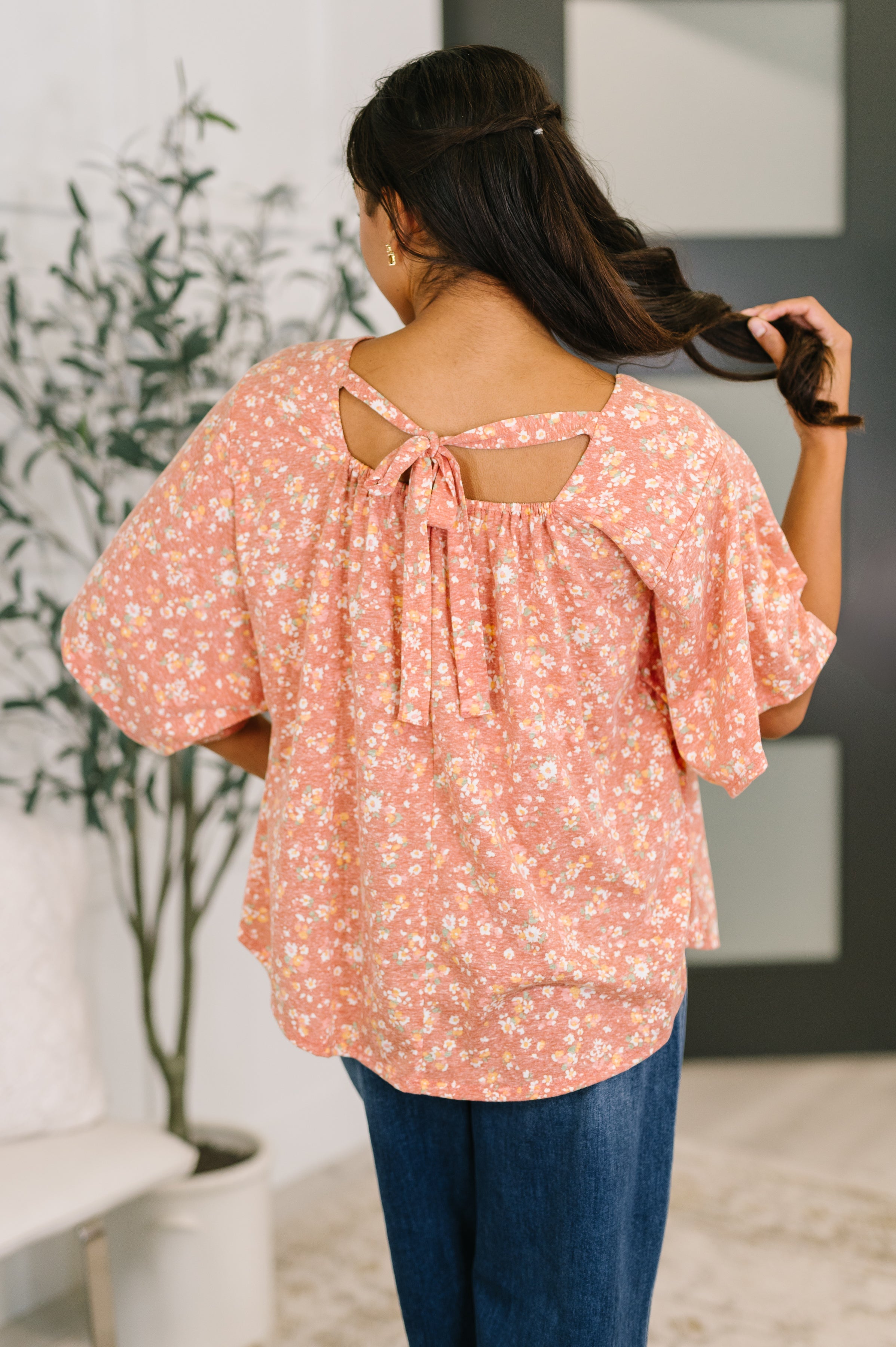 Woman with dark hair wearing a loose pink floral top with a bow detail at the back and relaxed short sleeves