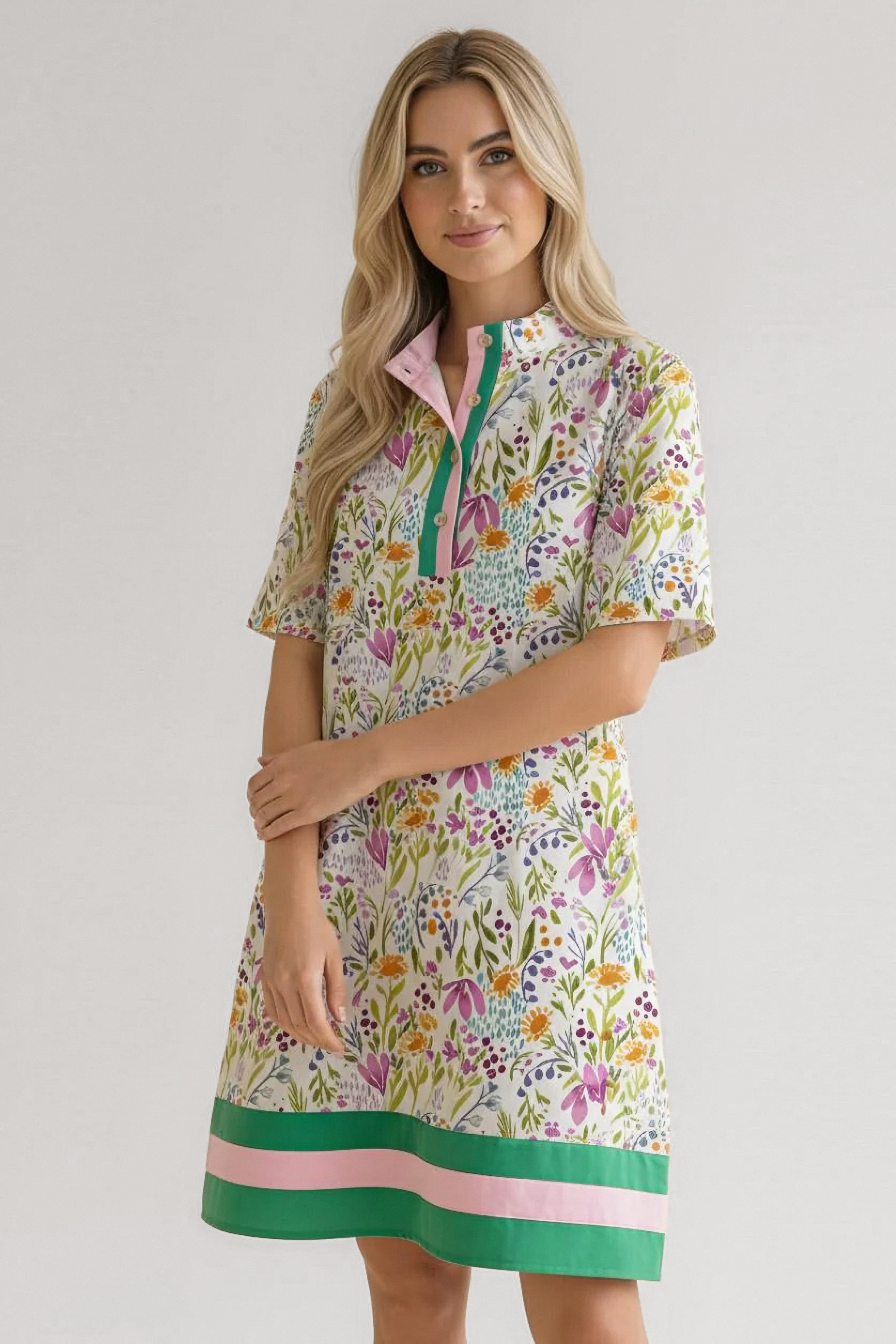Woman wearing floral short-sleeve dress with green and pink striped hem and green button placket standing with arms crossed