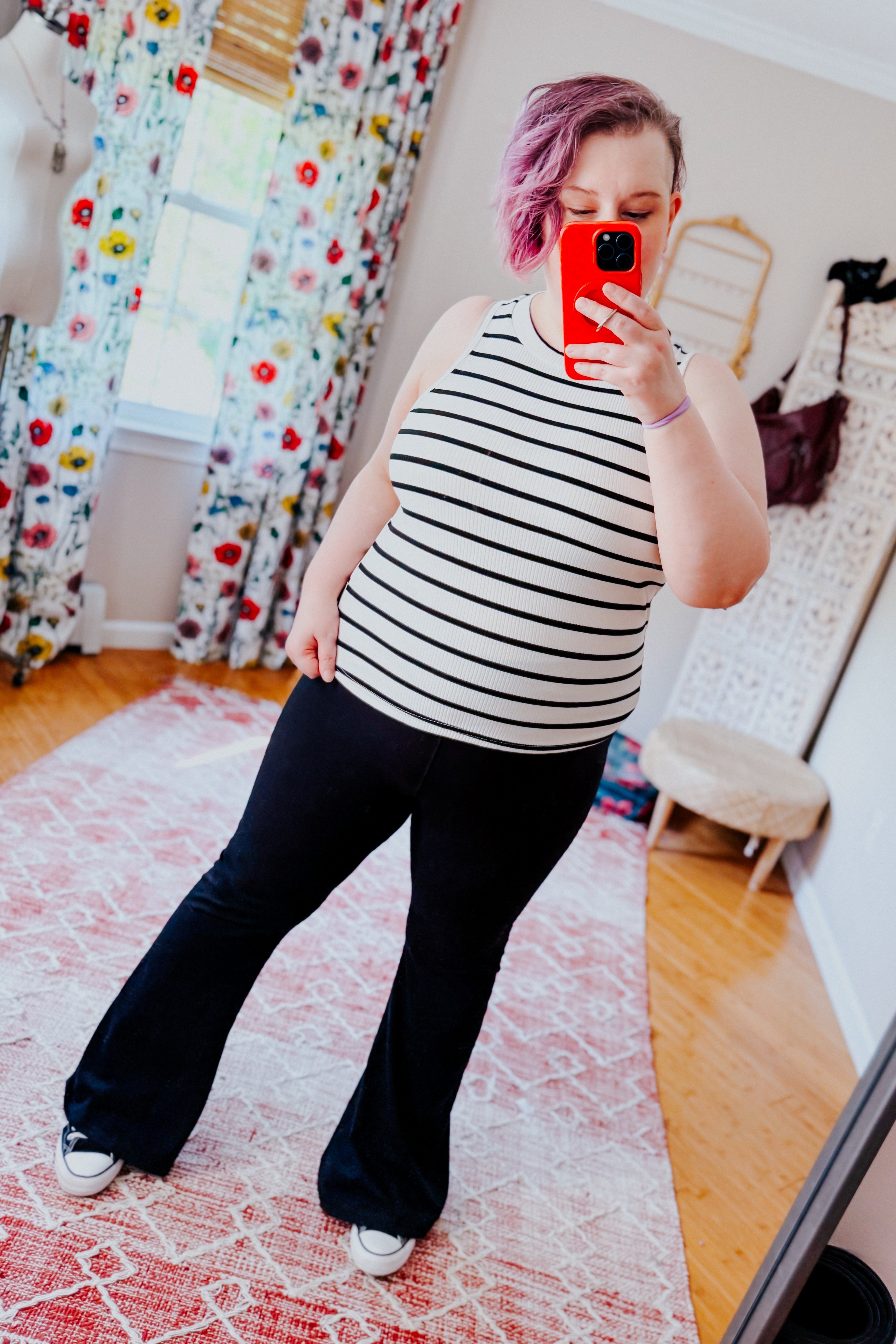 Woman wearing ivory striped ribbed halter tank with black flared pants and casual sneakers indoors