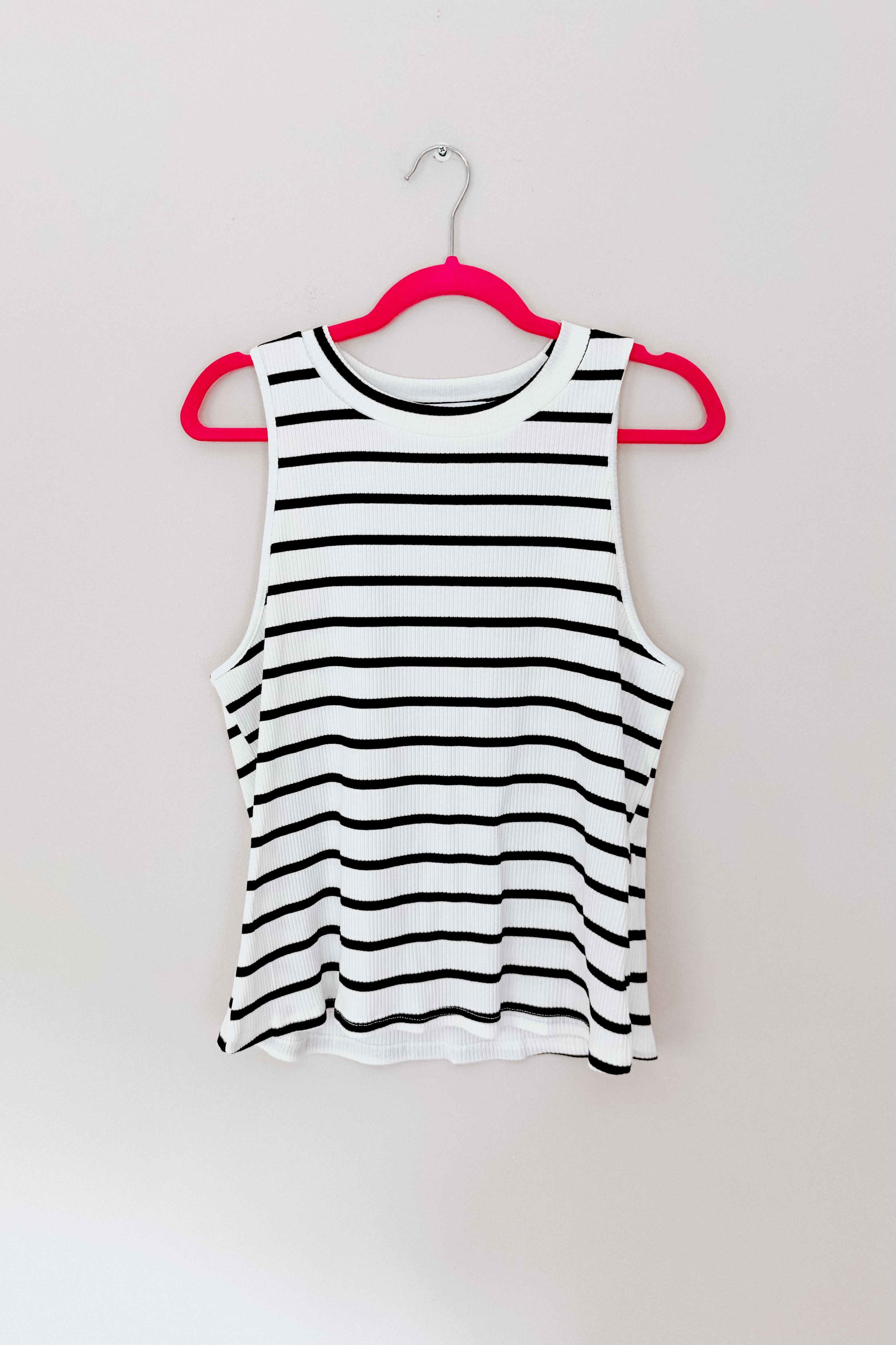 Ivory ribbed halter tank with horizontal black stripes hanging on bright pink hanger against light wall